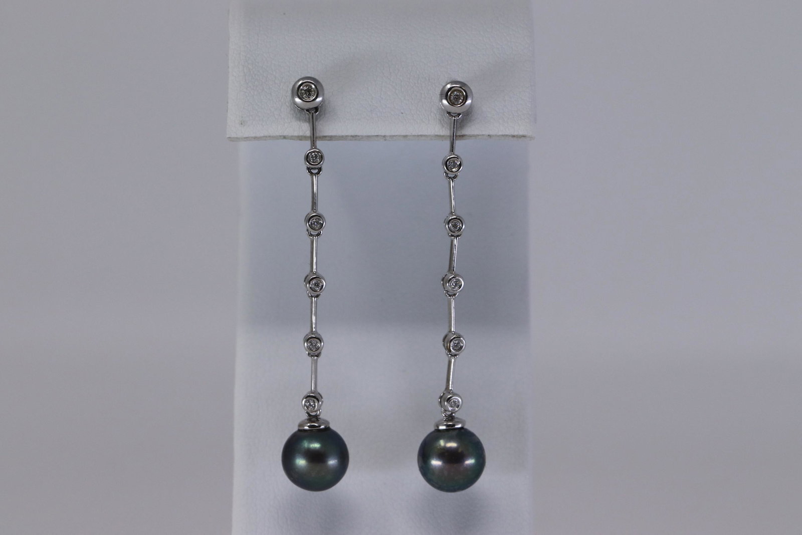 14Kt Dangling Diamond | Pearls Earrings: A ladies 14kt White Gold Diamond earrings. The earrings are Dangling style with diamonds and Pearls. There are a total of 12 round brilliant diamonds and 2 Black Pearls. Length: 2.00". Total weight: 3