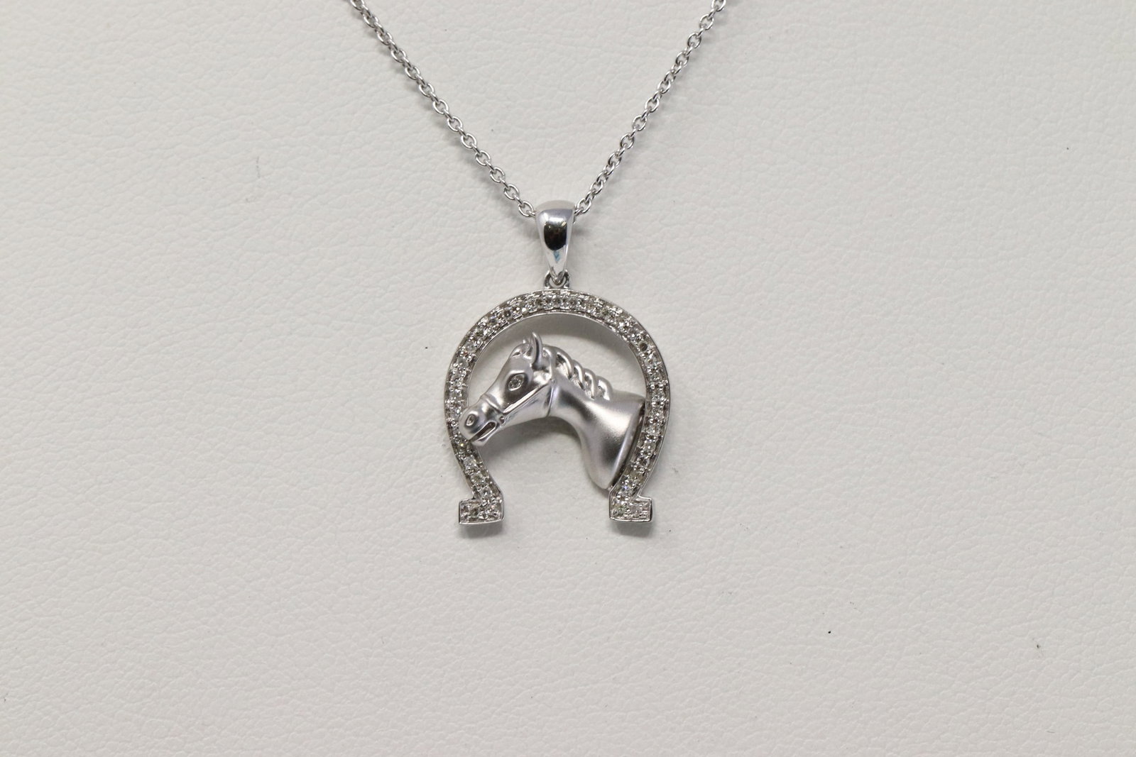 14Kt Gold Horse Shoe Necklace: A 14kt White Gold Diamond Horse and Shoe Pendant. Pendant has round brilliant diamonds weighting 0.19ctw. Necklace length: 18.00in. Total weight 4.10 grams. SKU: OD-NE8VNA