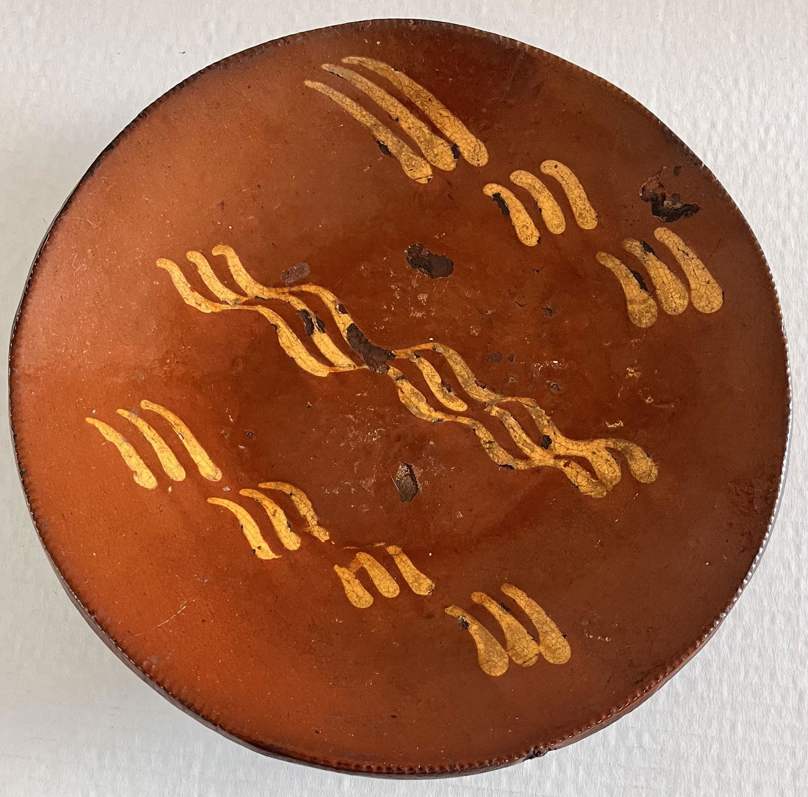 19TH C. SLIP DECORATED REDWARE PLATE: 19TH C. SLIP DECORATED REDWARE PLATE WITH YELLOW SLIP DECORATION - COGGLED EDGE - GOOD OVERALL CONDITION - NO CRACKS - GLAZE LOSS TO INTERIOR - 10 1/4" DIAMETER