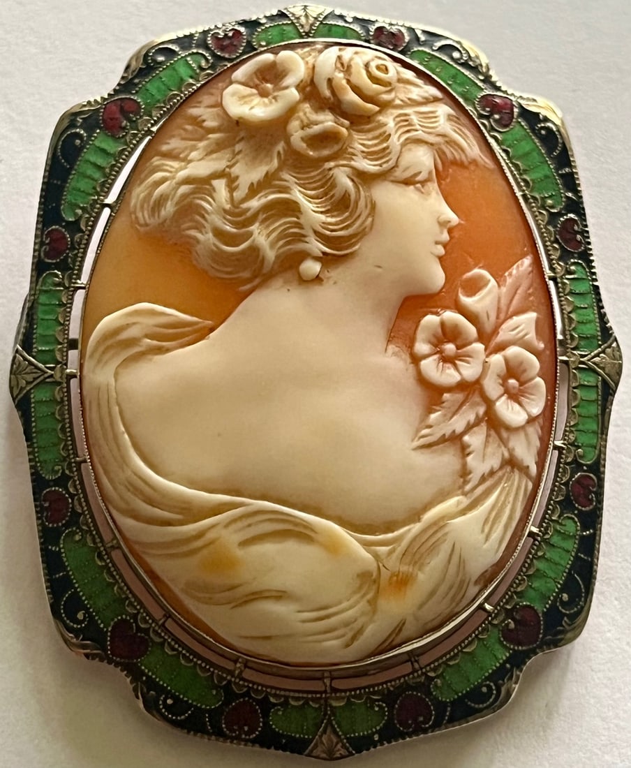 Large Antique Art Nouveau Carved Shell Cameo Brooch with Enamel work: Large Antique Art Nouveau Hand Carved Shell Cameo Brooch depicting a Classical Woman in profile with flowers in her hair and at her shoulder, Elaborate mount with vibrant green, black and red champlev