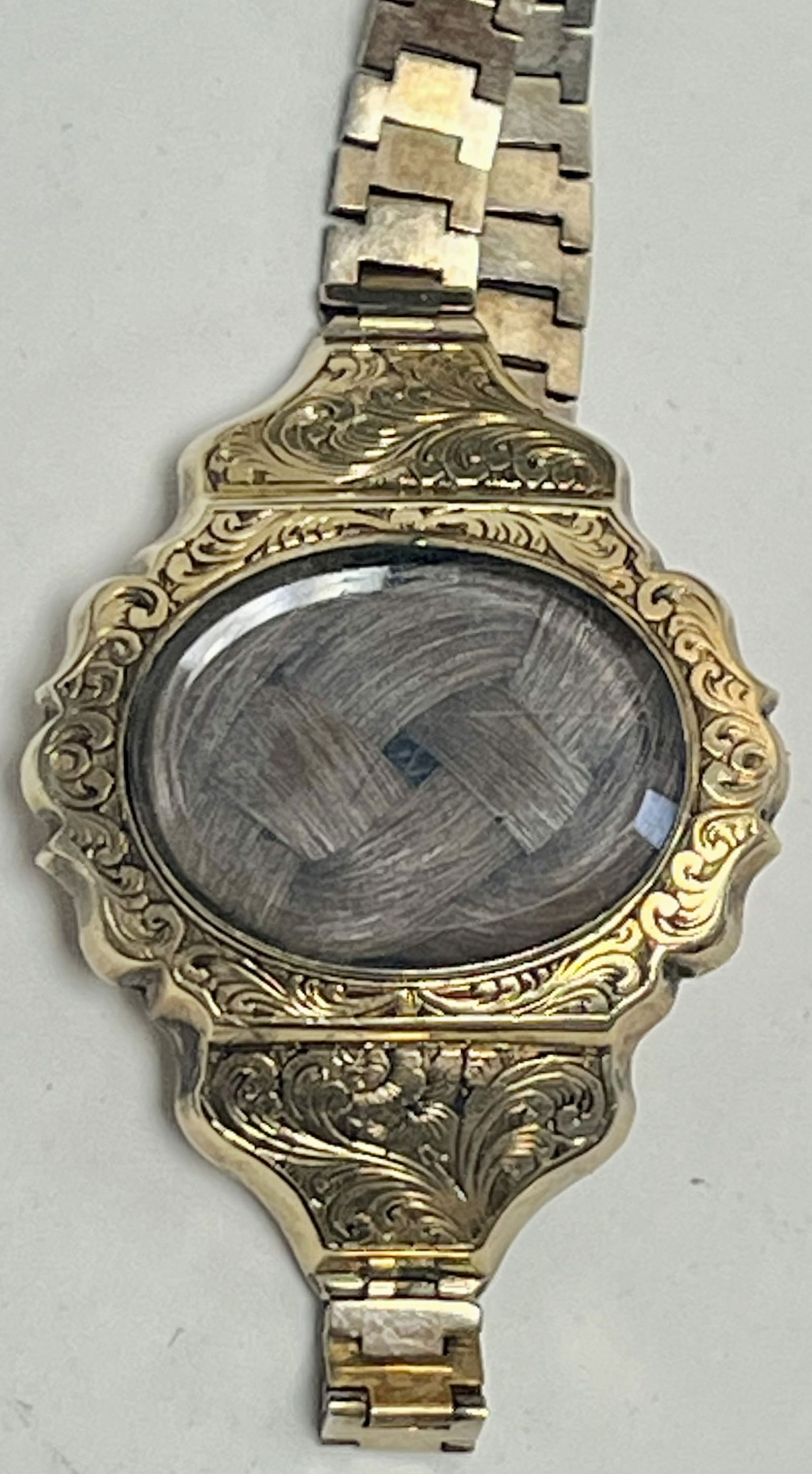 Victorian Gold-Filled Engraved Hairwork Locket Bracelet, c. 1870–1890: Antique Victorian-era gold-filled bracelet featuring an oval glass-covered hairwork locket centerpiece. The bracelet is richly engraved throughout with ornate scroll and foliate motifs on the locket f