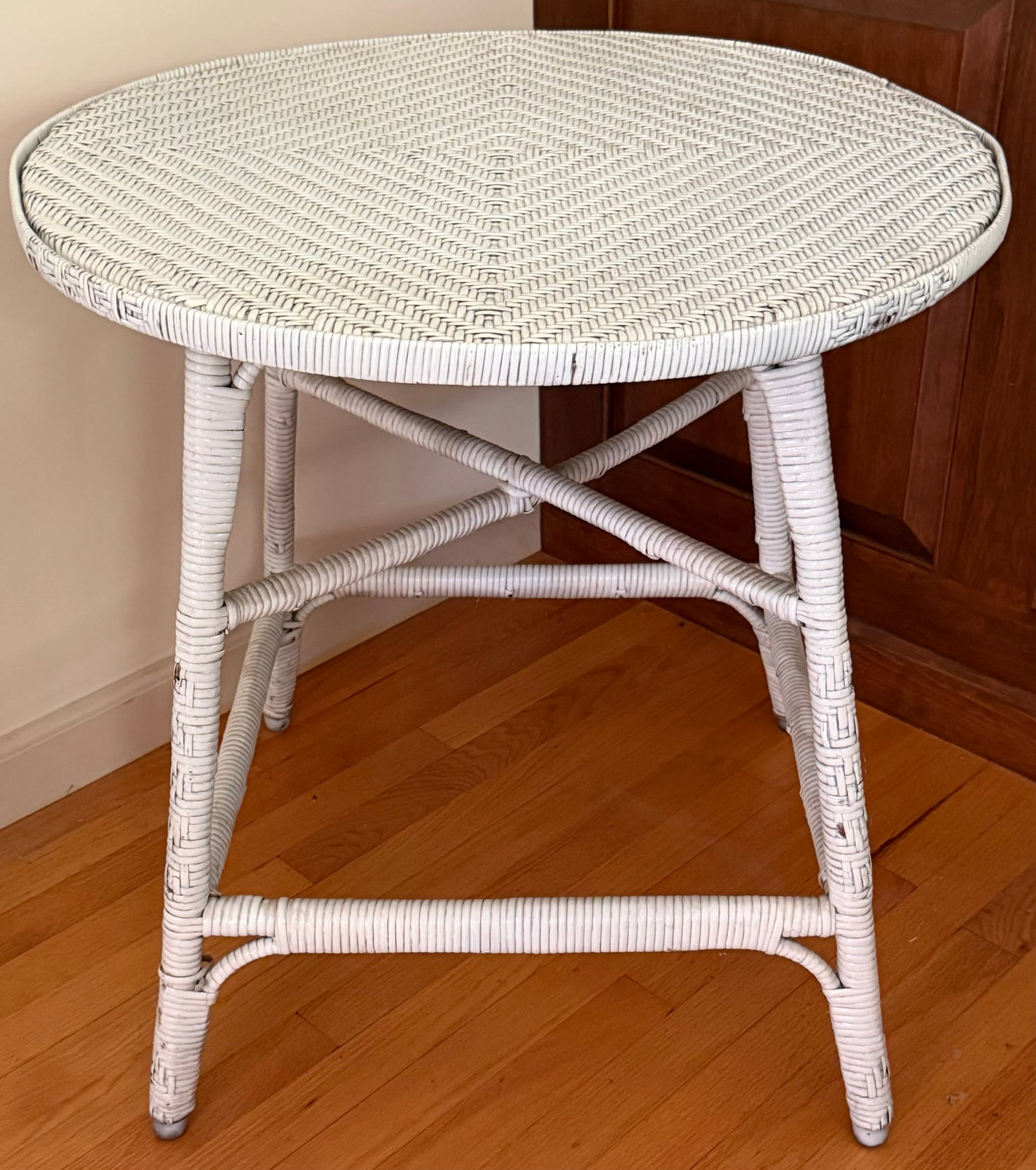 Vintage White Painted Wicker Round Occasional Table: Vintage round wicker and rattan occasional or side table, featuring a tightly woven herringbone-pattern top with concentric geometric design. Raised on four wrapped legs joined by horizontal
