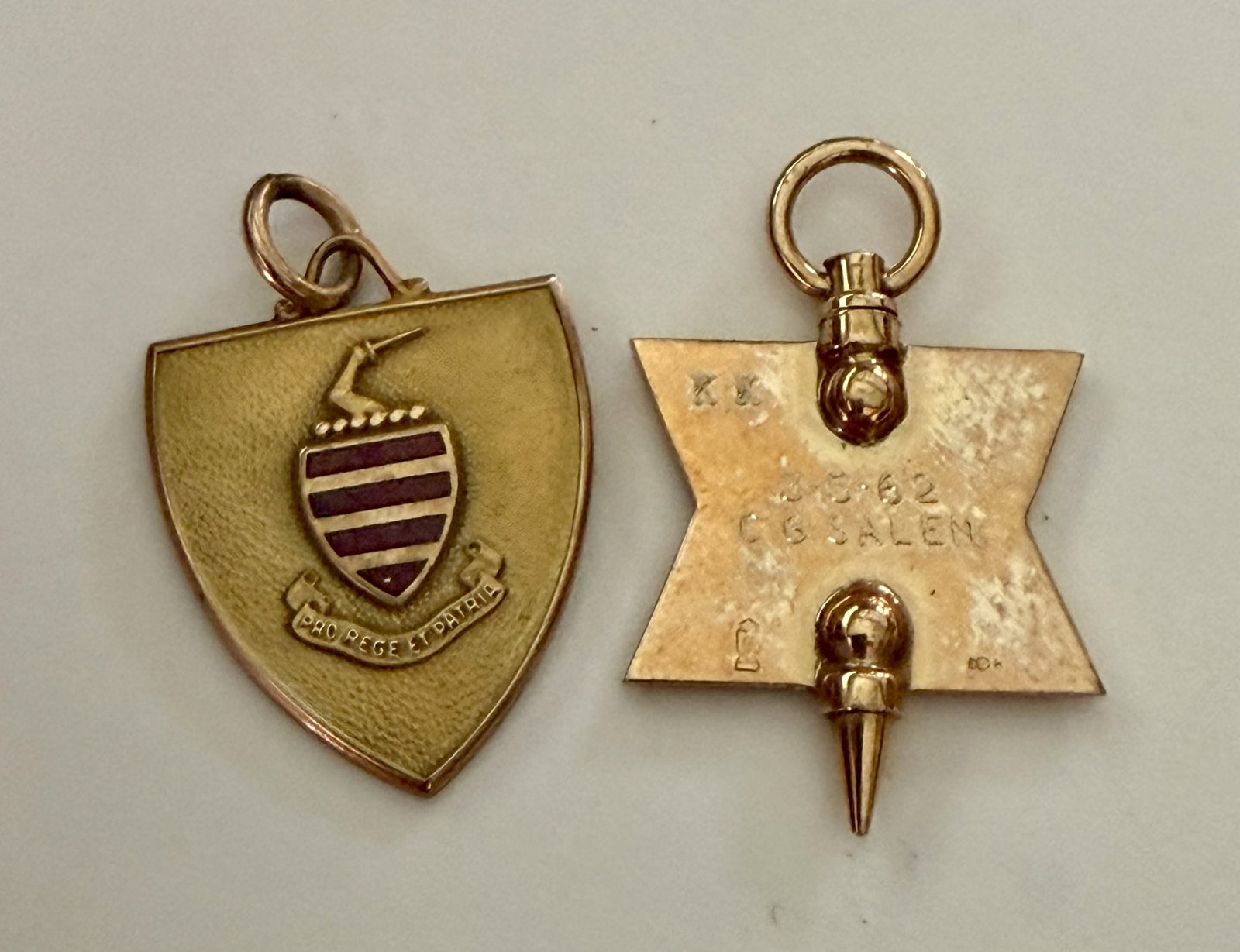 Two Vintage 10K Gold Fraternal & School Pendants, 1962: Lot of two vintage 10K gold pendants/charms, both dating to 1962. Includes a shield-form school or organizational pendant with applied red enamel heraldic crest featuring an antelope/deer head and