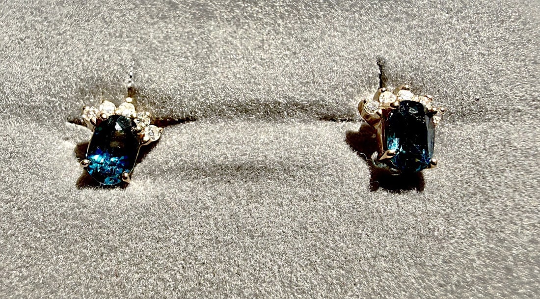 Pair 14K Gold Blue Topaz & Diamond Stud Earrings – 1.27 Grams: Attractive pair of fine jewelry stud earrings, each featuring a faceted oval deep blue gemstone, likely blue topaz, accented above by a cluster of small round brilliant-cut diamonds. Prong-set in