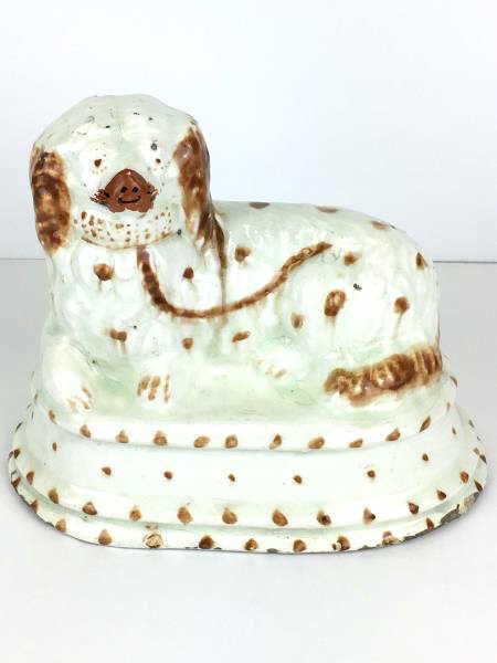 Folk Art Dog Statue: Folk Art Dog Statue reclining on cushion, porcelain, white with brown accents, chipped base, damaged face, craquelure, some green areas under glaze, 9 1/2" x 6" base x 8" h