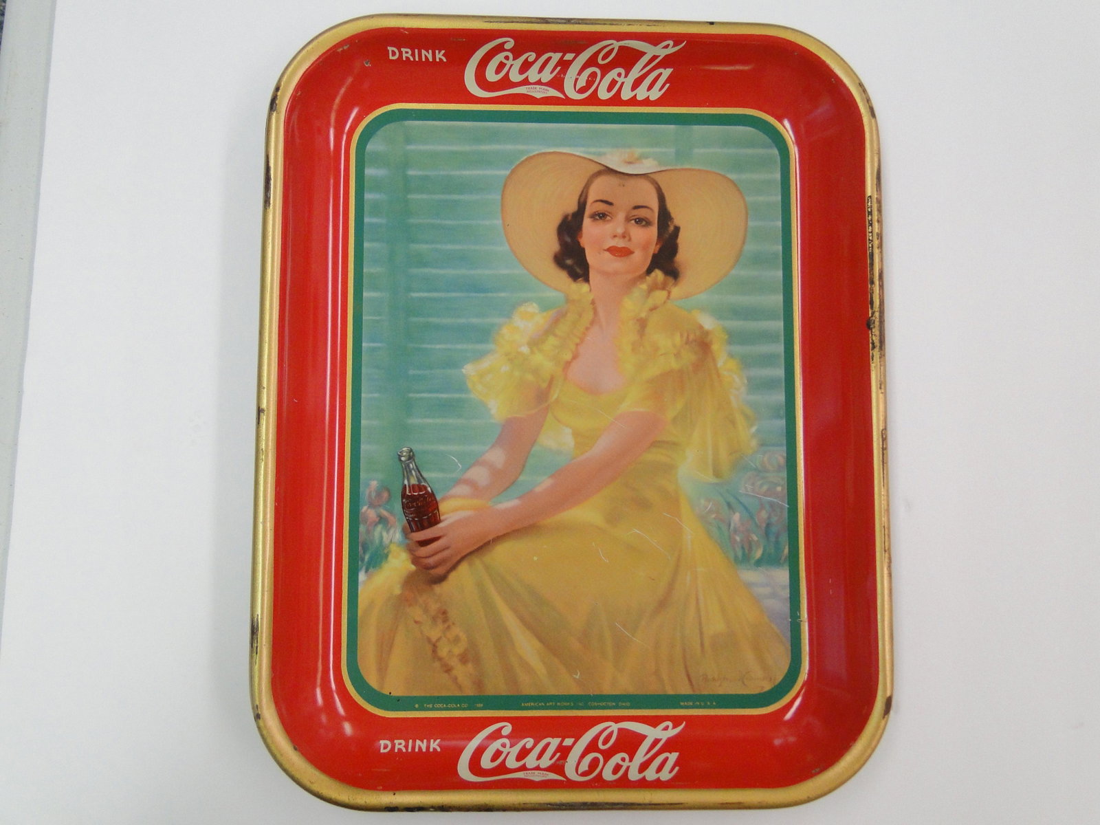 1938 Coca-Cola Serving Tray: woman in yellow dress with cape and hat, trademark in the tail of the C, artist signed lower right "Bradgbow Crandell", in lower border "The Coca-Cola Co 1938 American Artworks Inc Coshocton, Ohio Mad