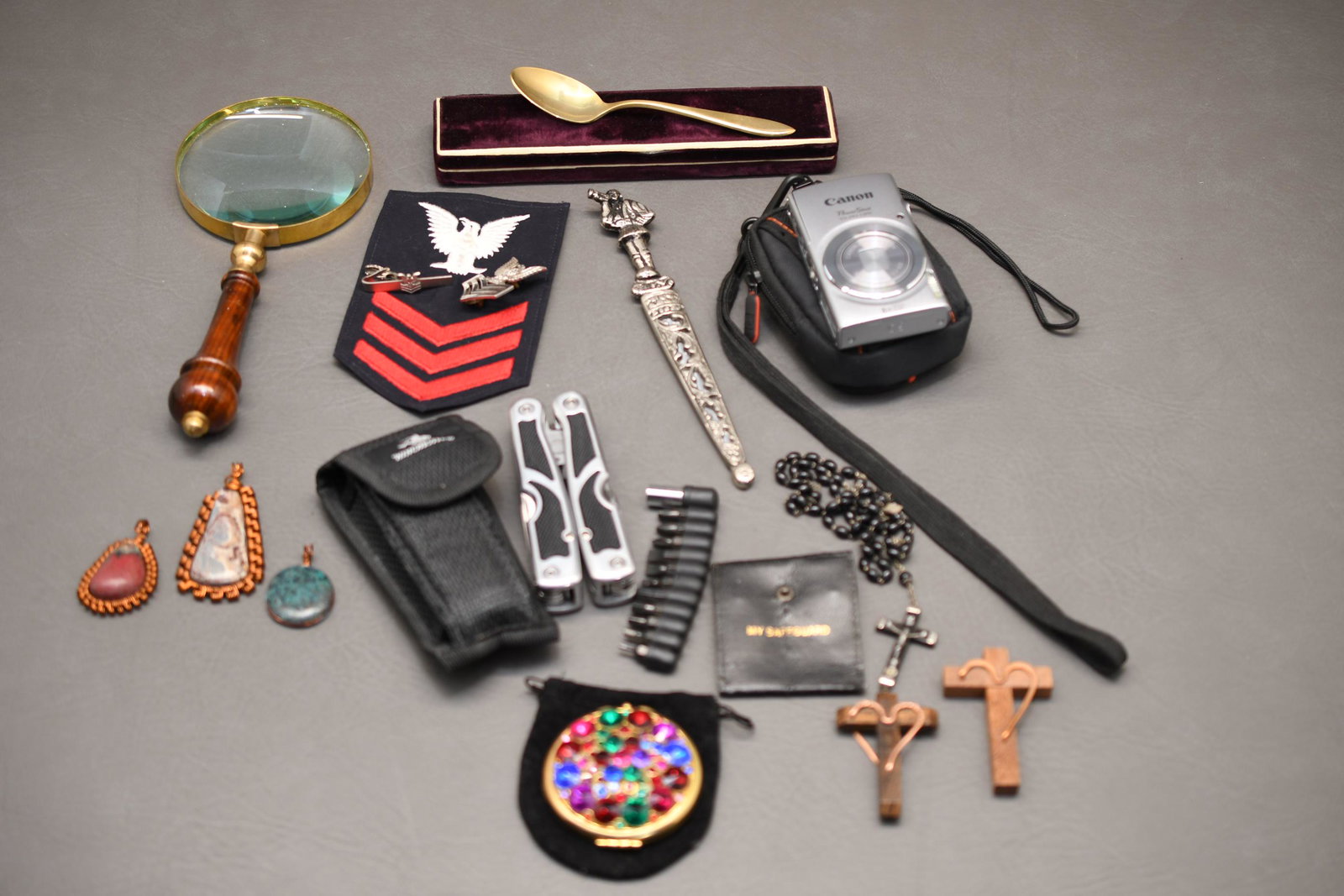 Box Lot: Canon Power shot camera, Winchester multi-tool, rosary set, Dirilyte spoon, letter opener, military patch and pins, magnifying glass, Katherine's Collection Compote, 3 necklace pendants, approximate t