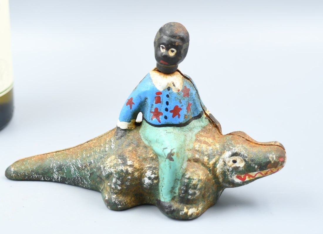 Cast Iron Bank Boy on Allegator: Vintage cast iron Bank Boy riding an Alligator, boy's head rotates. Height- 3 1/2". Length-6". Weight- 14oz. (NOTE-Weight and dimensions are before packaging)