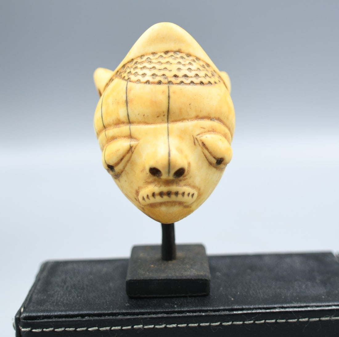 Antique African Bone Mask Pendant: African mask pendant carved from bone. (NOTE-Weight and dimensions are before packaging) pendant-2 1/4"L x 1 1/2"D x 1 3/4"W. Stand base-1"x 1 1/4"x 1/4". Total height-3 1/4". Combined weight-3.9oz.