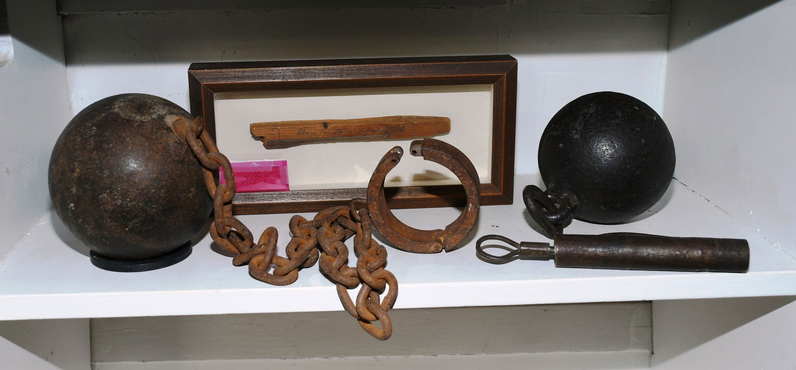 Slavery Artifacts: Slavery Artifacts. 1 Screw lock shackle, 1 cast iron ball w/ chain loop, 1 cast iron ball with chain and shackle, 1 piece of wood from a Slave Mart in Charlotte, S.C. from 1866, in a shadow box. (NOTE