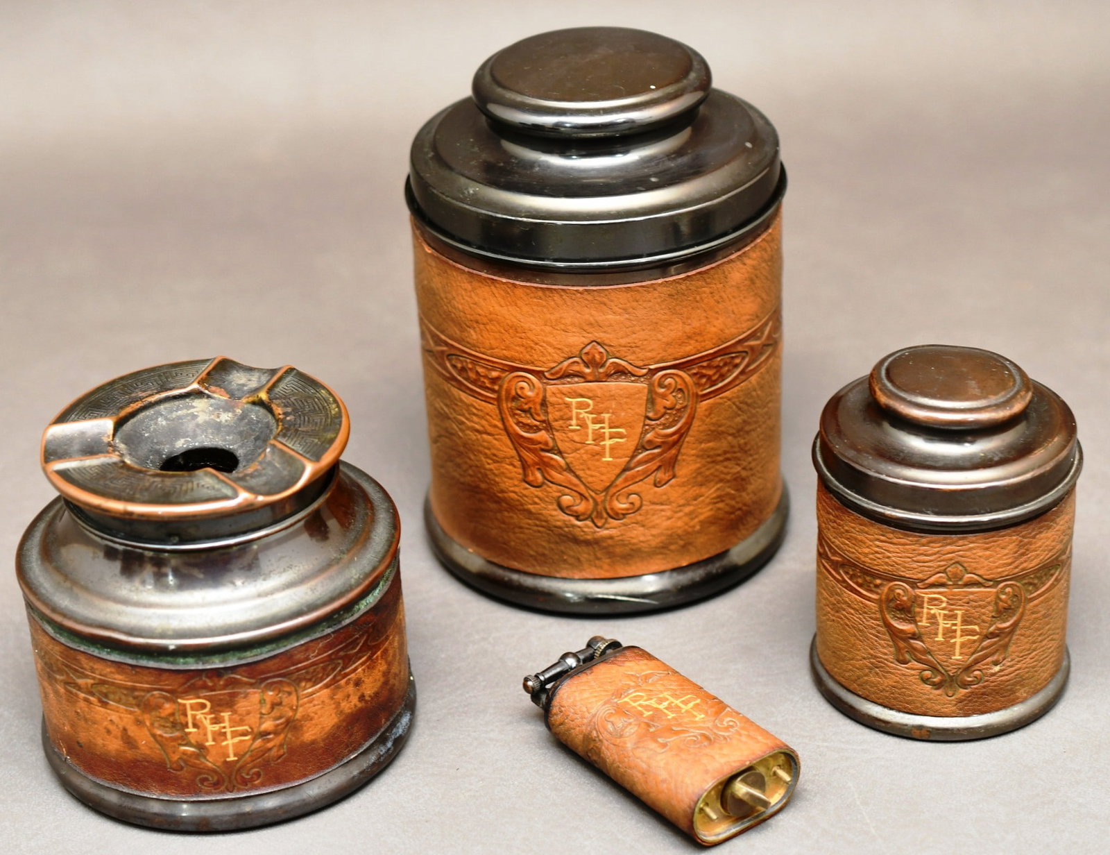 Smokers set: Cigar humidor, cigarette humidor, ashtray, & lighter made of brass with a bronze finish, the lighter takes lighter fluid. There is a makers stamp in the leather wrap, but we can't quite make it out. D