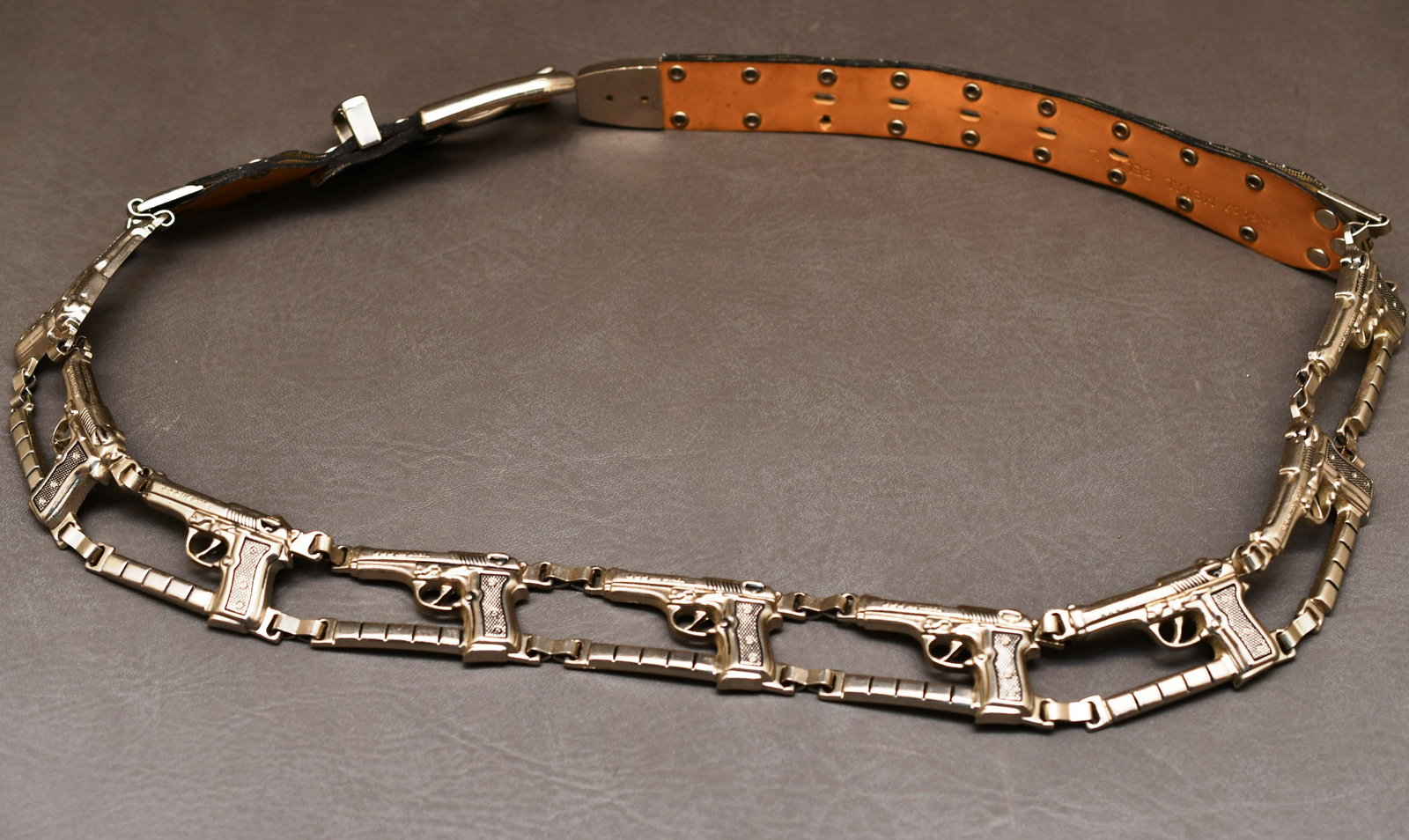 Novelty Metal Hand Gun Waist Belt: Belt with 9 Semi Automatic hand guns that read 123 Model with 3 stars, each gun is 2" x 1-1/2", The rivets holding the synthetic strap sections are made to look like bullets, and the overall length of