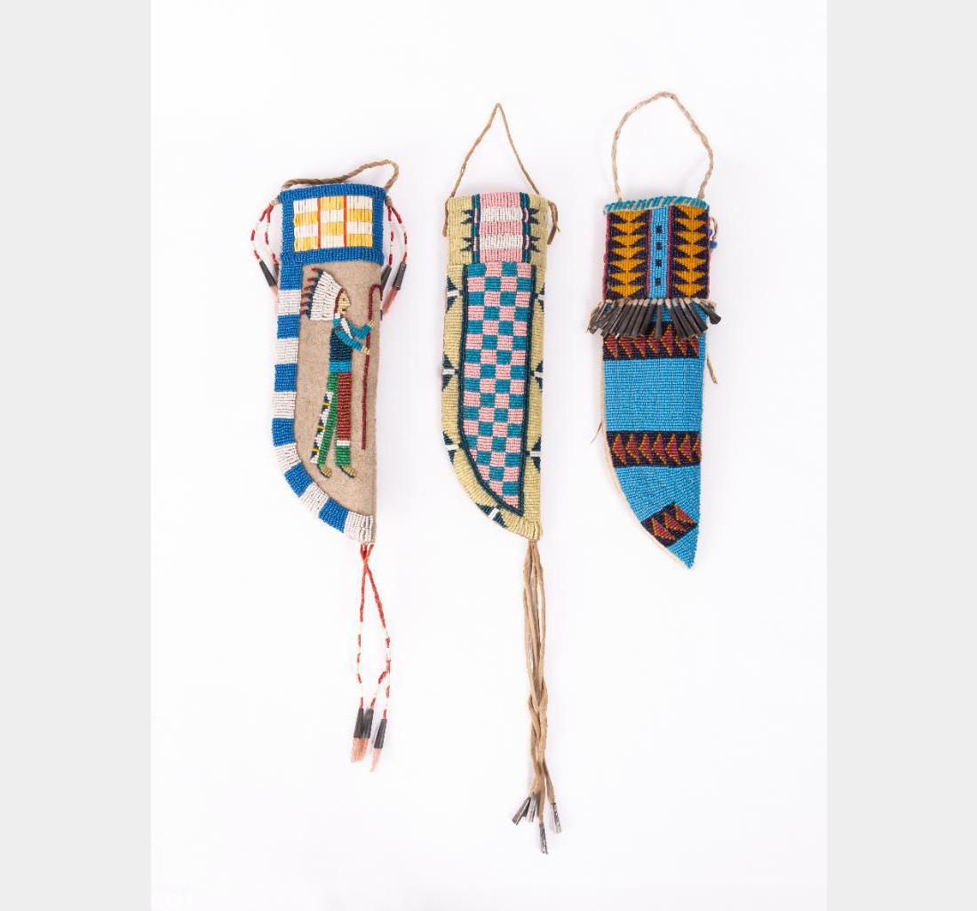 Group of three Beaded Knife Sheaths: Group of three Beaded Knife Sheaths Largest is 11" x 3". Two have drops and all are accented with tin cones. Varying designs on each, including one with an Indian and headdress. Contemporary. $600-900