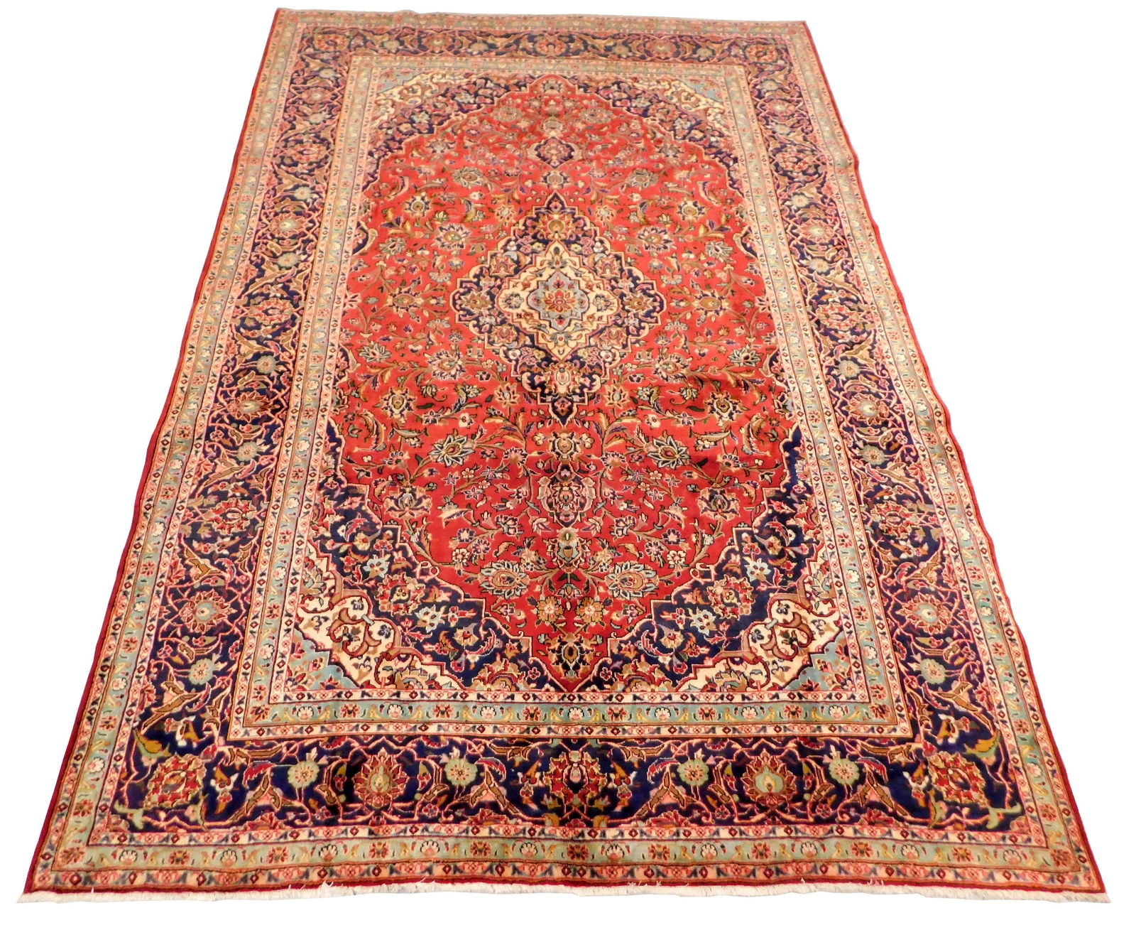 RUG: Semi-Antique Persian Kashan, 9' x 13' 2", soft red: RUG: Semi-Antique Persian Kashan, 9' x 13' 2", soft red field, ensconced in wide navy floral border, sky blue guard borders, gold, rose, taupe, wheat accents. [PLEASE BRING APPROPRIATE ASSISTANCE AND