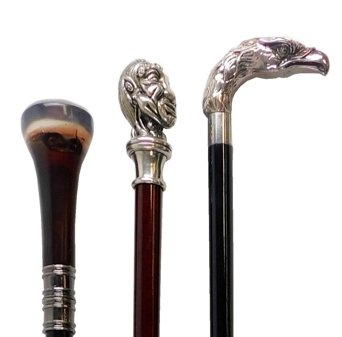 Three walking sticks: Sterling silver eagle head handle, black lacquer tapered base, 36" l.; erotic: Three walking sticks: Sterling silver eagle head handle, black lacquer tapered base, 36" l.; erotic knob top walking stick with cast metal handle, female bodies comprise a man's face, 36" l.; and a hi