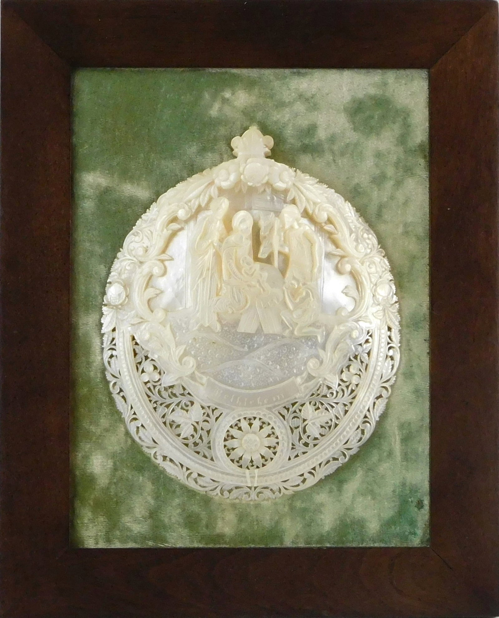 Mother-of-Pearl carved shell plaque, 20th C., elaborately carved full shell with central vignette of: Mother-of-Pearl carved shell plaque, 20th C., elaborately carved full shell with central vignette of the Adoration of the Shepherds over a banner inscribed “Bethlehem” and encircled by floral 