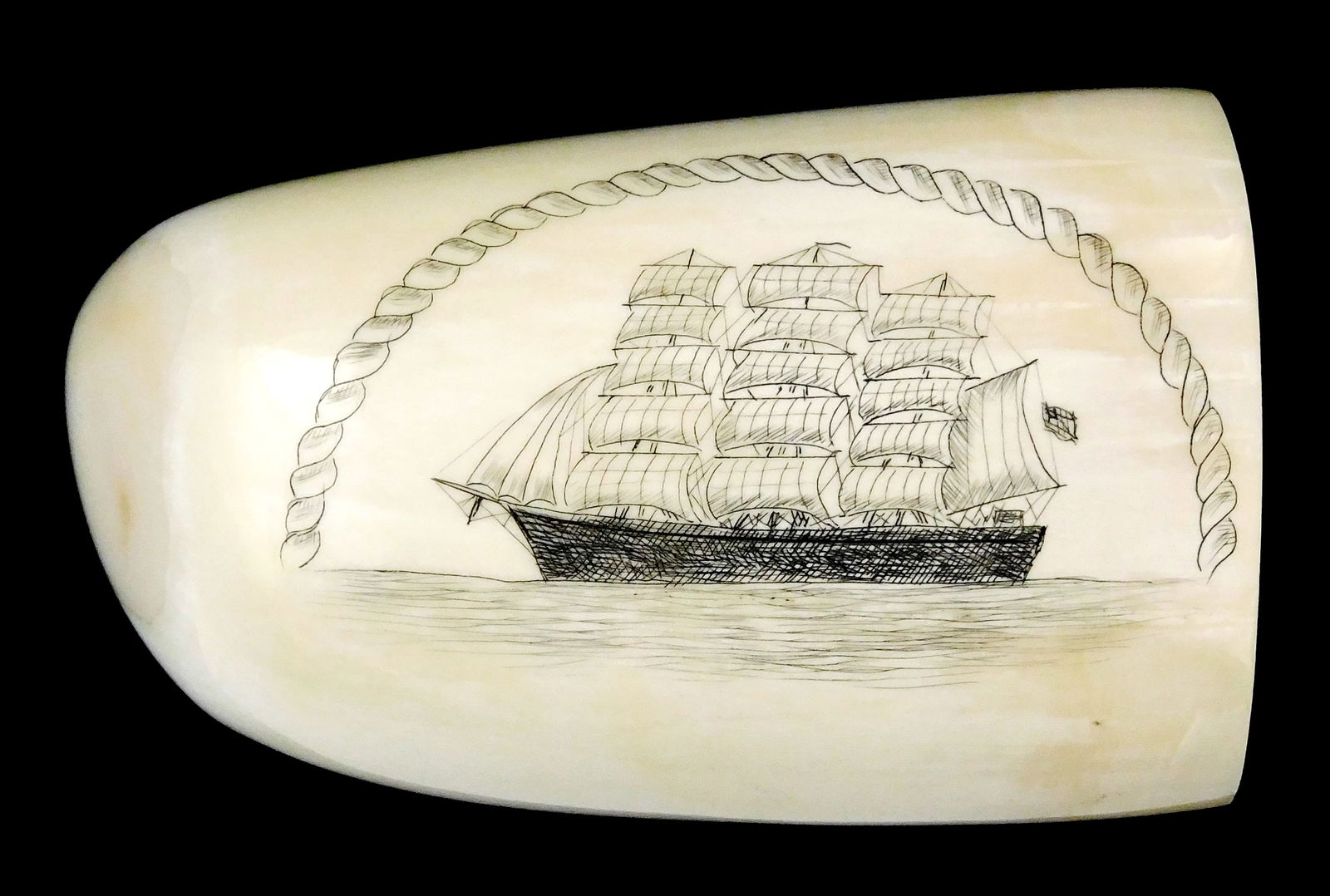 SCRIMSHAW: Engraved whale tooth with American ship decoration, profile of sailing ship with full: SCRIMSHAW: Engraved whale tooth with American ship decoration, profile of sailing ship with full sails and American flag, rope border, unsigned, wear consistent with age and use, sold as is, 3 3/4" l.