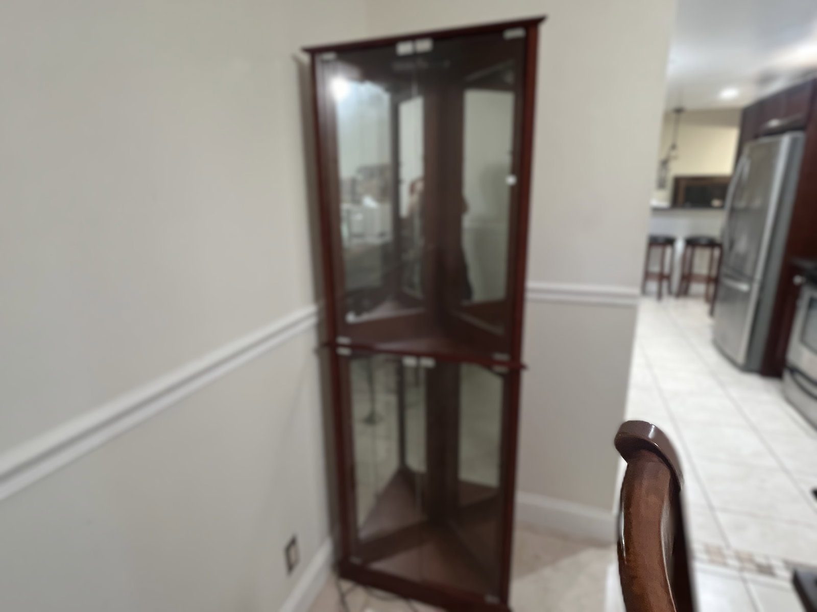 Contemporary Mahogany Finish Corner Curio Cabinet with Glass Panels: Corner curio cabinet featuring a triangular design with glass panels on the front and sides, ideal for space efficient display. The cabinet includes upper and lower compartments with hinged glass door