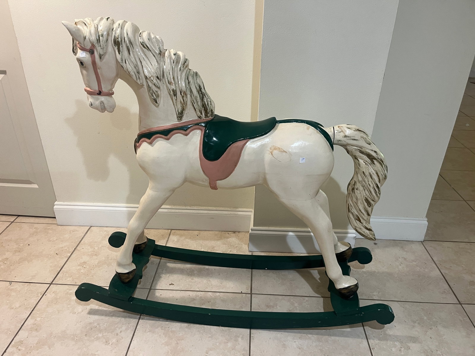 Hand-Painted Wooden Rocking Horse with Green Base and Saddle: Charming hand-painted wooden rocking horse featuring a cream body with carved mane and tail, accented in green and rose tones. The horse stands on a dark green curved rocker base and displays decorati