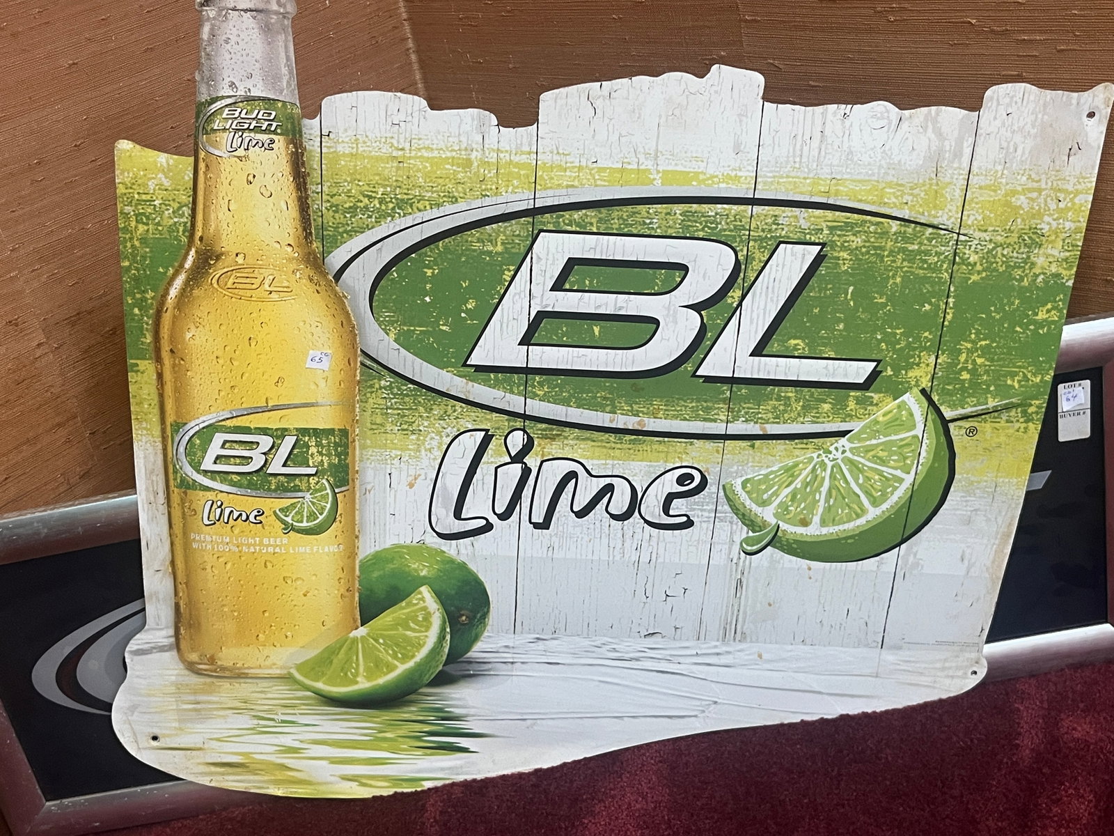 Bud Light Lime Die-Cut Tin Advertising Sign, 29 x 30 In.: Large Bud Light Lime die-cut tin advertising sign featuring a chilled Bud Light Lime bottle, fresh lime wedges, and the "BL Lime" logo set against a rustic wood plank graphic. Constructed of printed t