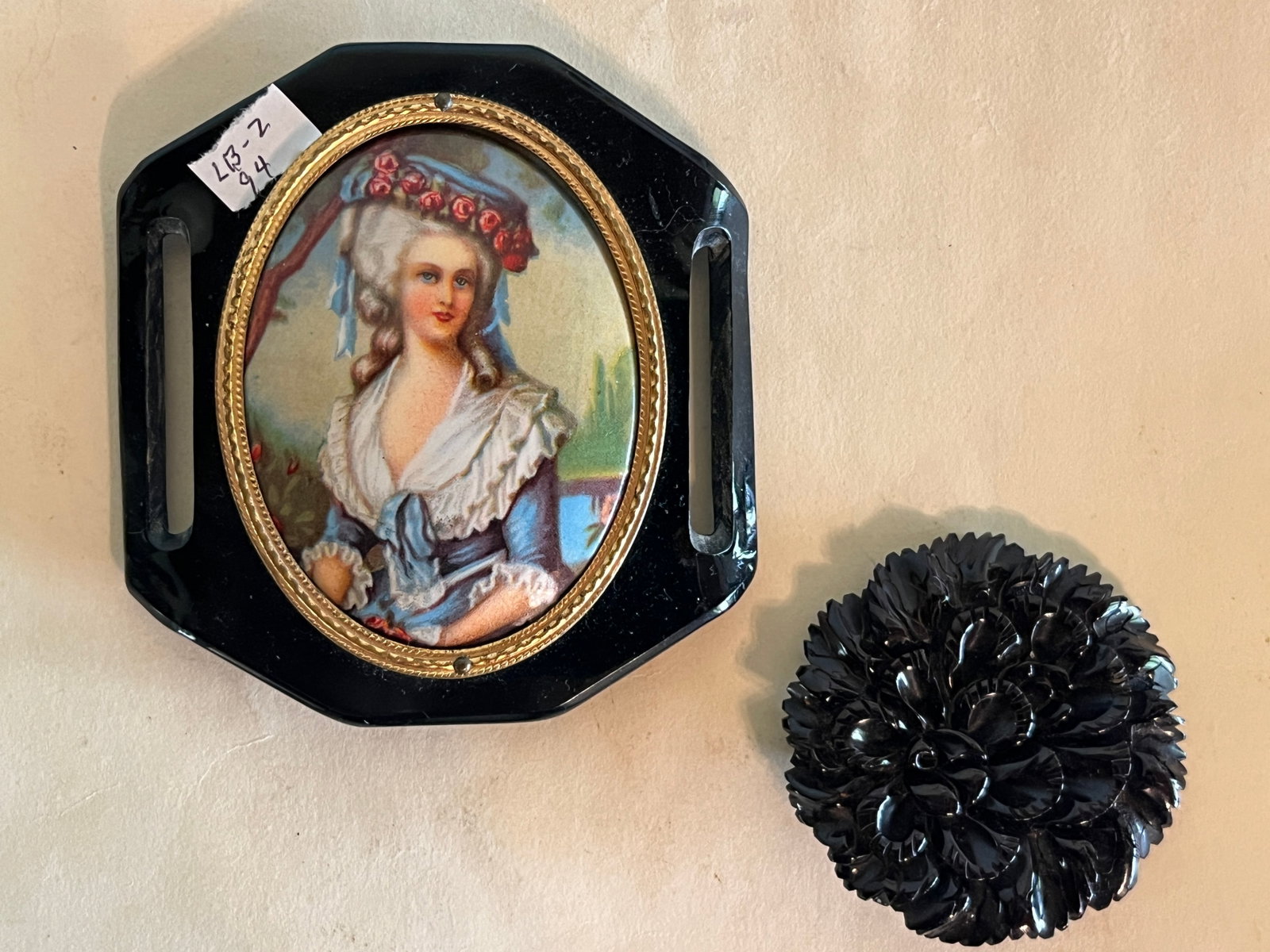 Pair of Vintage Black Plastic Accessories Portrait Buckle & Floral Brooch: A pair of vintage molded black plastic accessories, comprising: Rectangular buckle inset with an oval printed portrait of an 18th century lady framed in gilt, with slotted sides for ribbon or belt att