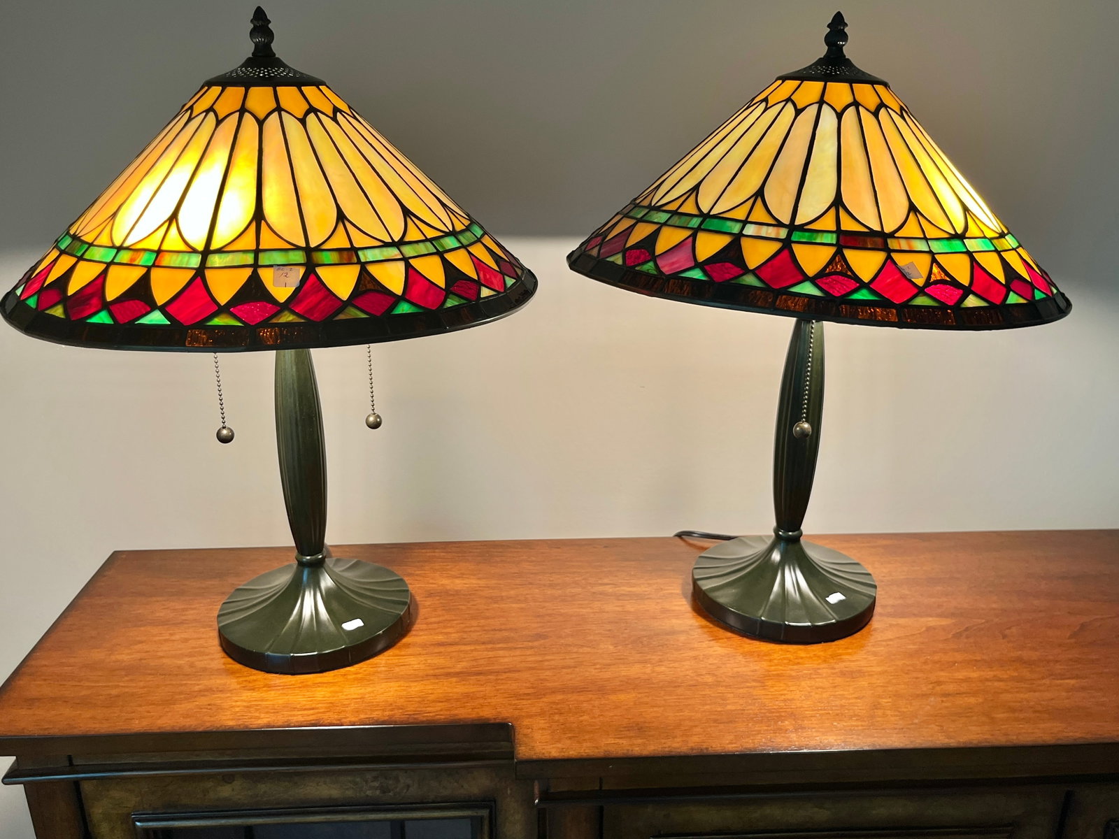 Pair of Quoizel Tiffany-Style Stained Glass Table Lamps, 22"H x 16.5"W: Beautiful matching pair of Quoizel table lamps featuring hand-crafted stained glass shades in a vibrant geometric pattern of amber, red, green, and cream tones. Each lamp rests on a fluted antique bro