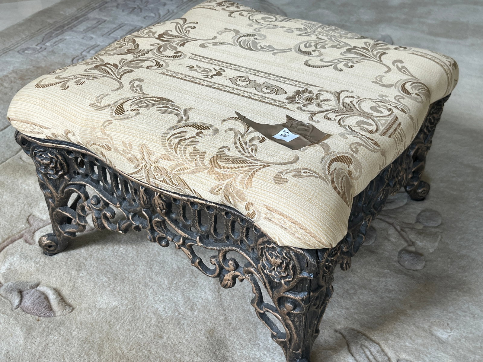 Victorian Style Cast Iron Ottoman with Upholstered Top, 18" W ? 18" D ? 12" H: A decorative Victorian?style ottoman featuring an ornate cast iron base with pierced floral and scroll motifs and claw feet. The cushioned top is upholstered in a beige damask fabric with raised folia
