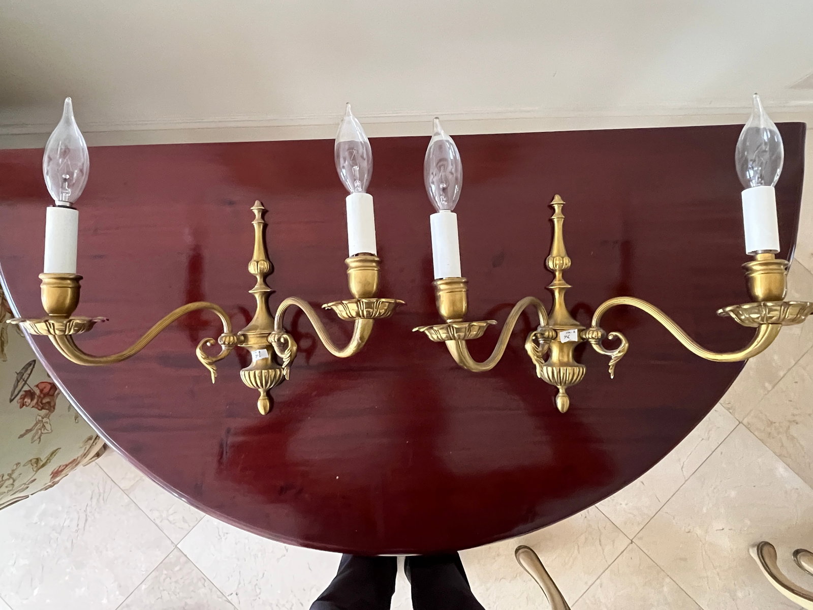 Pair of Brass Two-Arm Wall Sconces, 8.5" H ? 12" W: Elegant pair of solid brass wall sconces, each featuring two scrolling arms with candle?style sockets and decorative bobeches. The central column is fluted and topped with a finial, complemented by cl