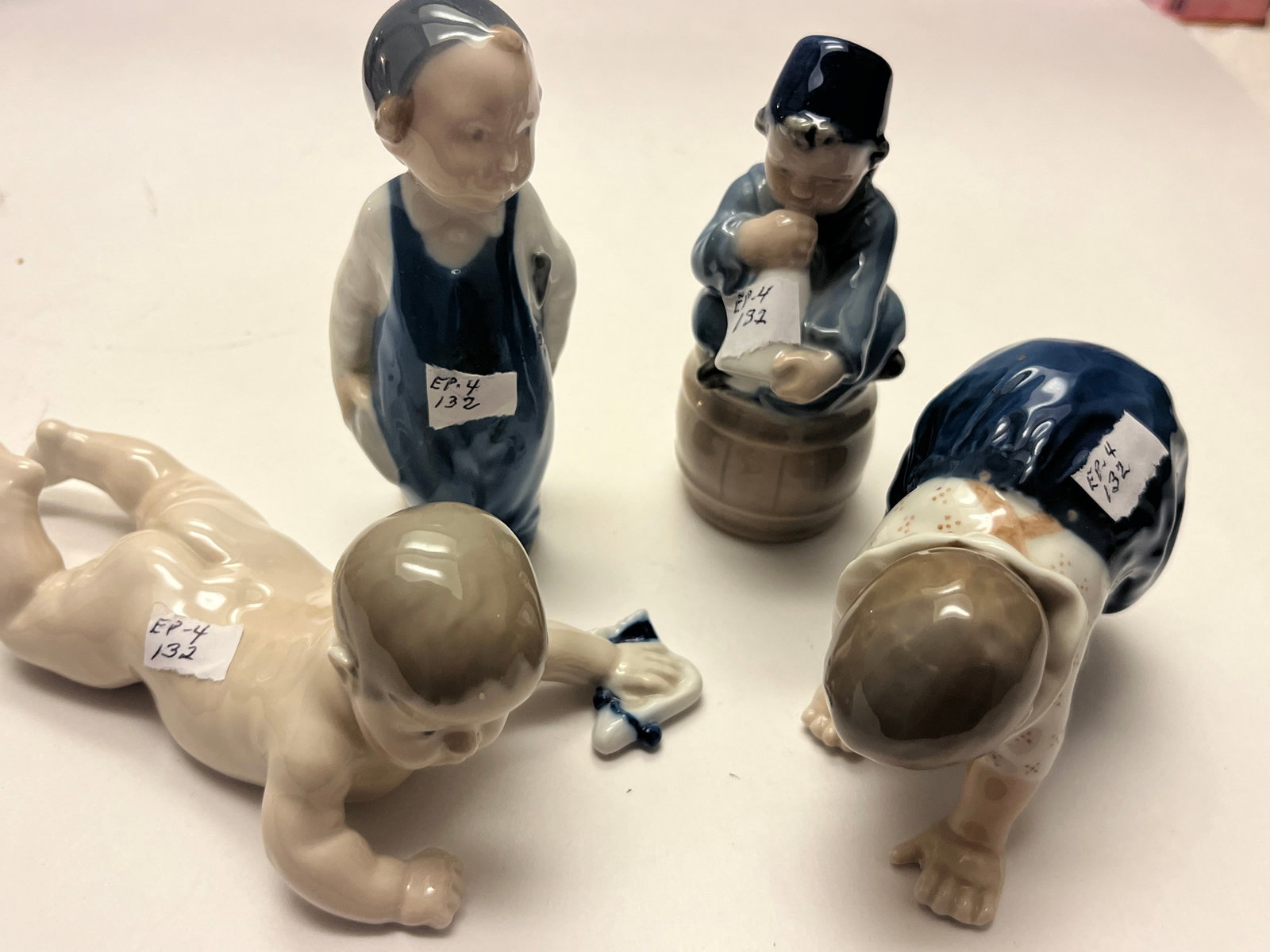 Four Royal Copenhagen Porcelain Child Figurines, Sold as One Lot: Group of four Royal Copenhagen porcelain figurines depicting children in various poses, including a standing boy, a seated child drinking from a bottle while perched on a barrel, and two crawling todd