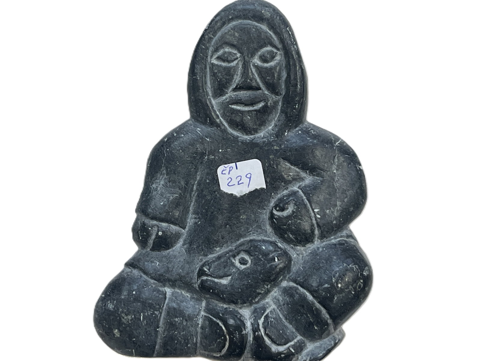 Vintage Canadian Inuit Carved Stone Hunter with Seal, Signed/Tagged, 5.5"H x 4"W x 1.75"D: Vintage Canadian Inuit carved stone figural sculpture depicting a seated hunter holding a seal across his lap. Carved from dark gray/black stone with simplified, expressive facial features and incised