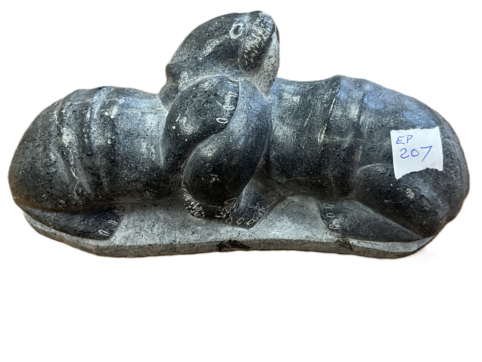 Inuit Soapstone Carving – Walrus,3h x 7w x 2.5d: Hand-carved soapstone sculpture depicting a walrus in a reclining pose, rendered with stylized form and incised detailing to tusks and flippers. The stone shows natural veining and tonal variation fro