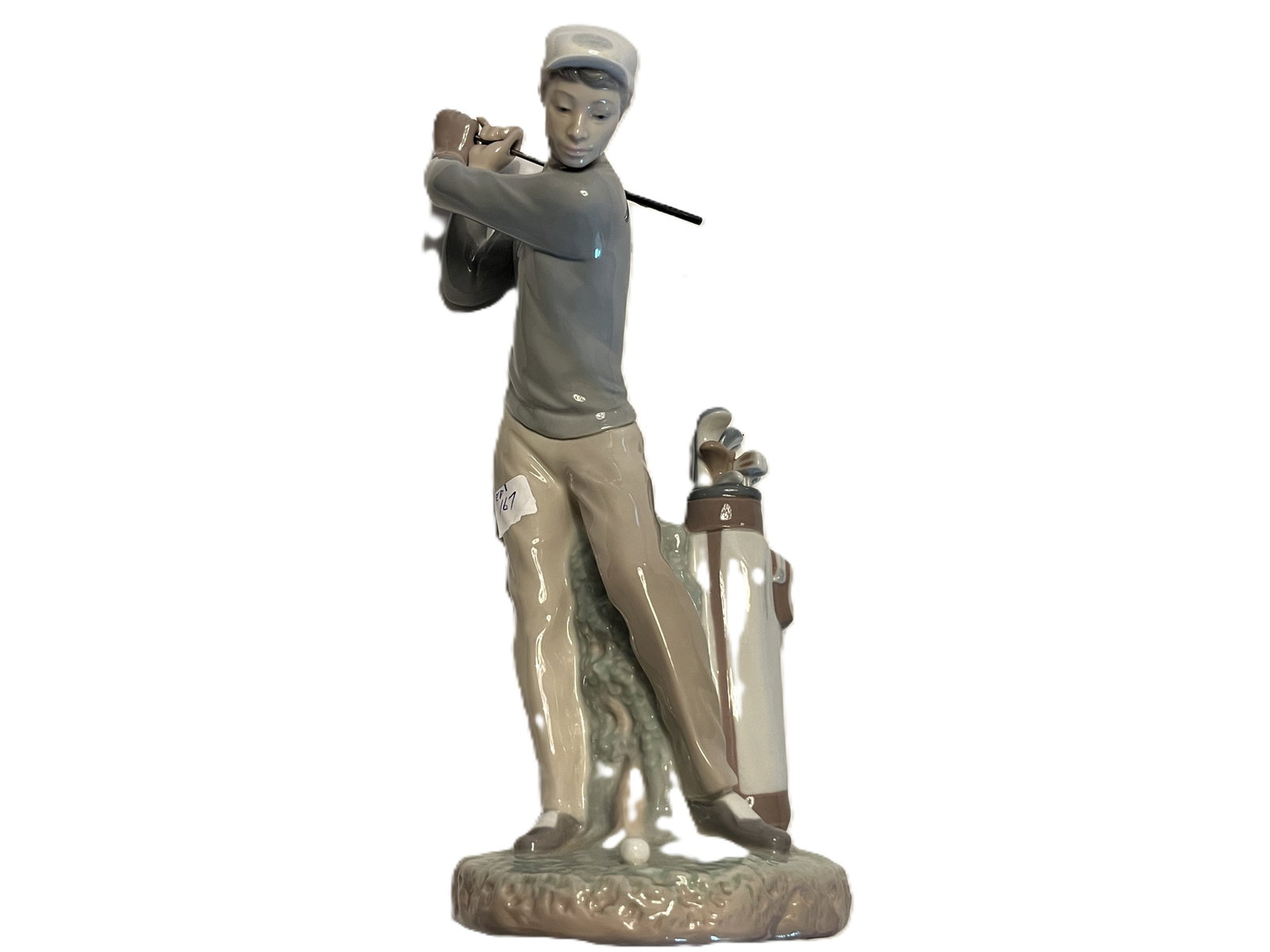 Lladró Porcelain Golfer Figurine with Golf Bag – Missing Golf Club: Lladró glazed porcelain figurine depicting a male golfer posed at the completion of his swing, accompanied by a detailed golf bag filled with clubs. Finished in Lladró's characteristic soft palette 
