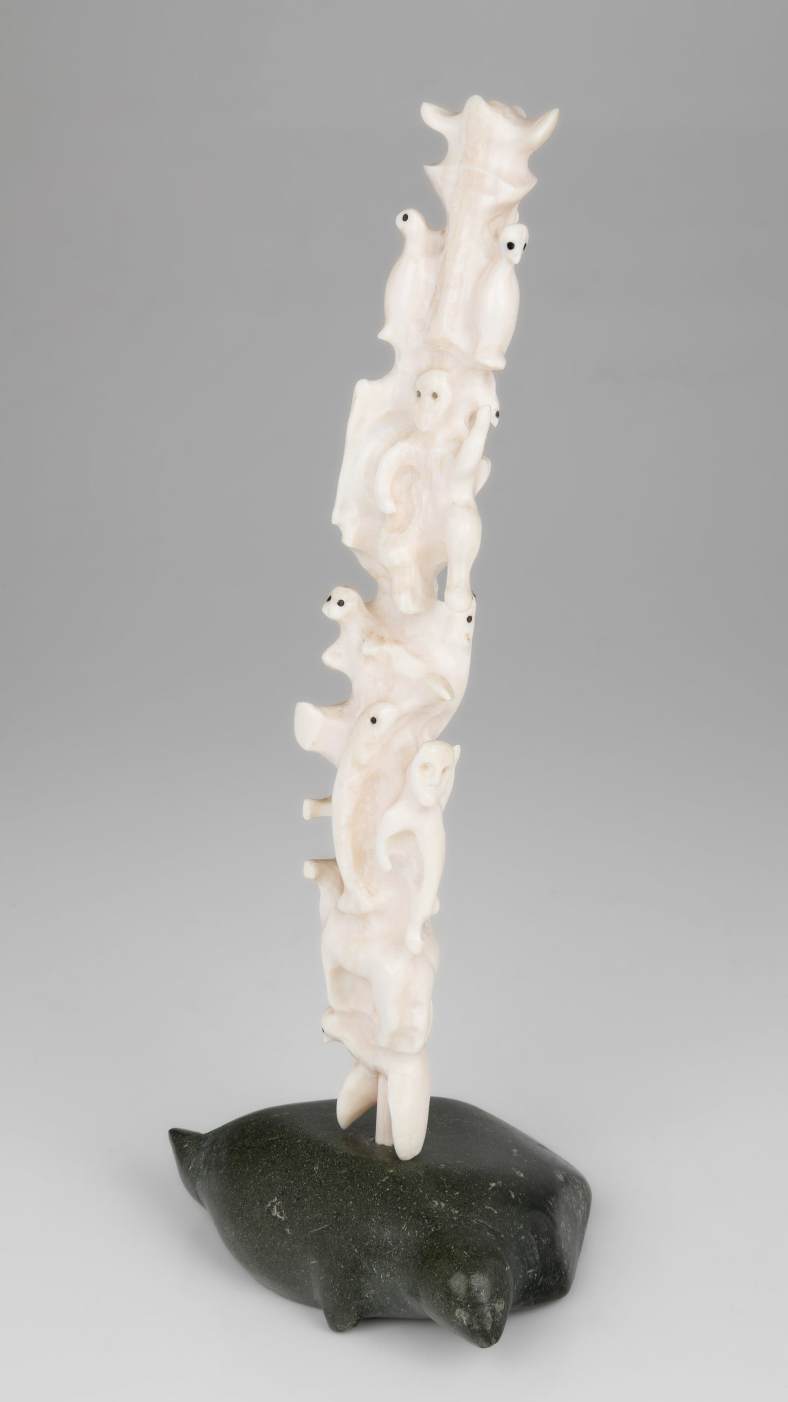 BERNADETTE IVALOOARJUK SAUMIK, INUIT, Totemic Composition with Inuit and Owls on Seal Base, 1977: BERNADETTE IVALOOARJUK SAUMIK (1938-) NAUJAAT (REPULSE BAY) / RANKIN INLET (KANGIQLINIQ) Totemic Composition with Inuit and Owls on Seal Base, 1977 tusk, stone, and black inlay, 11.25 x 4.75 x 3.5 in 