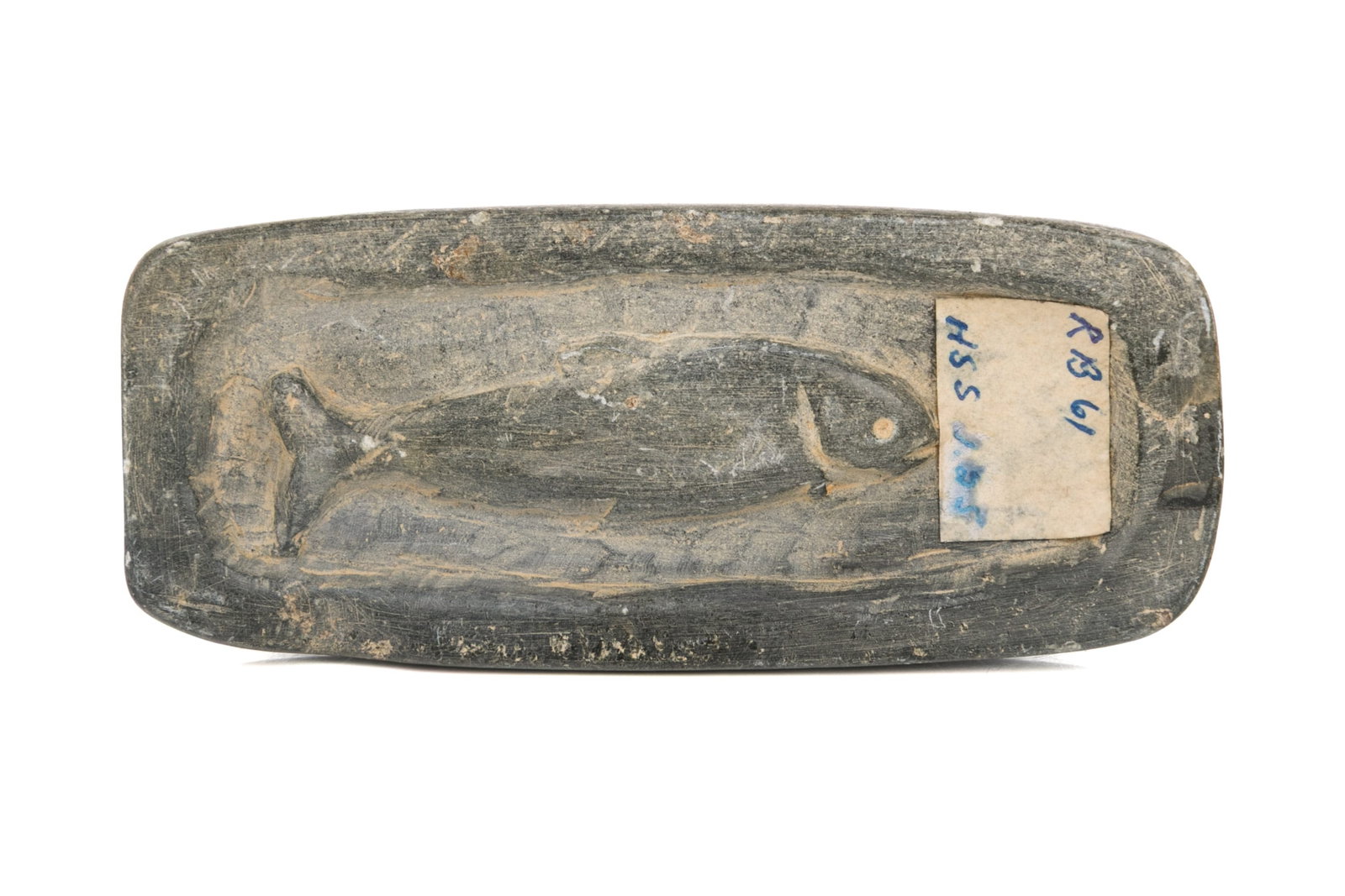 UNIDENTIFIED ARTIST, NAUJAAT (REPULSE BAY), Fish in a Cooking Pot, 1961: UNIDENTIFIED ARTIST, NAUJAAT (REPULSE BAY) Fish in a Cooking Pot, 1961 stone, 0.5 x 4 x 1.25 in (1.3 x 10.2 x 3.2 cm) unsigned; with affixed label from La Guilde (The Canadian Handicrafts Guild), in b