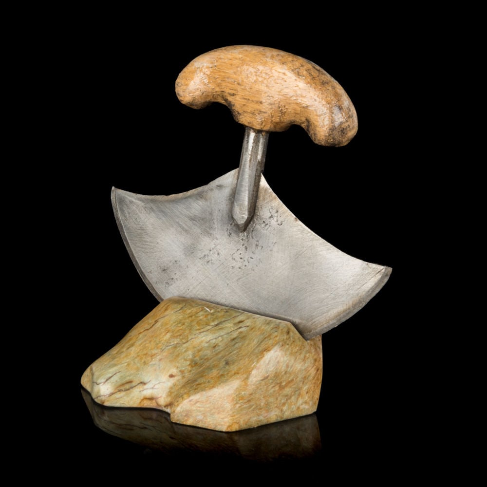 Probably PAULOOSIE MUCKPA, INUIT, Model Ulu with Rest, 2000s: Probably PAULOOSIE MUCKPA (1937-) IKPIARJUK (ARCTIC BAY) Model Ulu with Rest stone, metal, and wood, 5.25 x 5.25 x 3.5 in (13.3 x 13.3 x 8.9 cm) signed, "MUCKPAH". ESTIMATE: $200 — $400 Provenance: