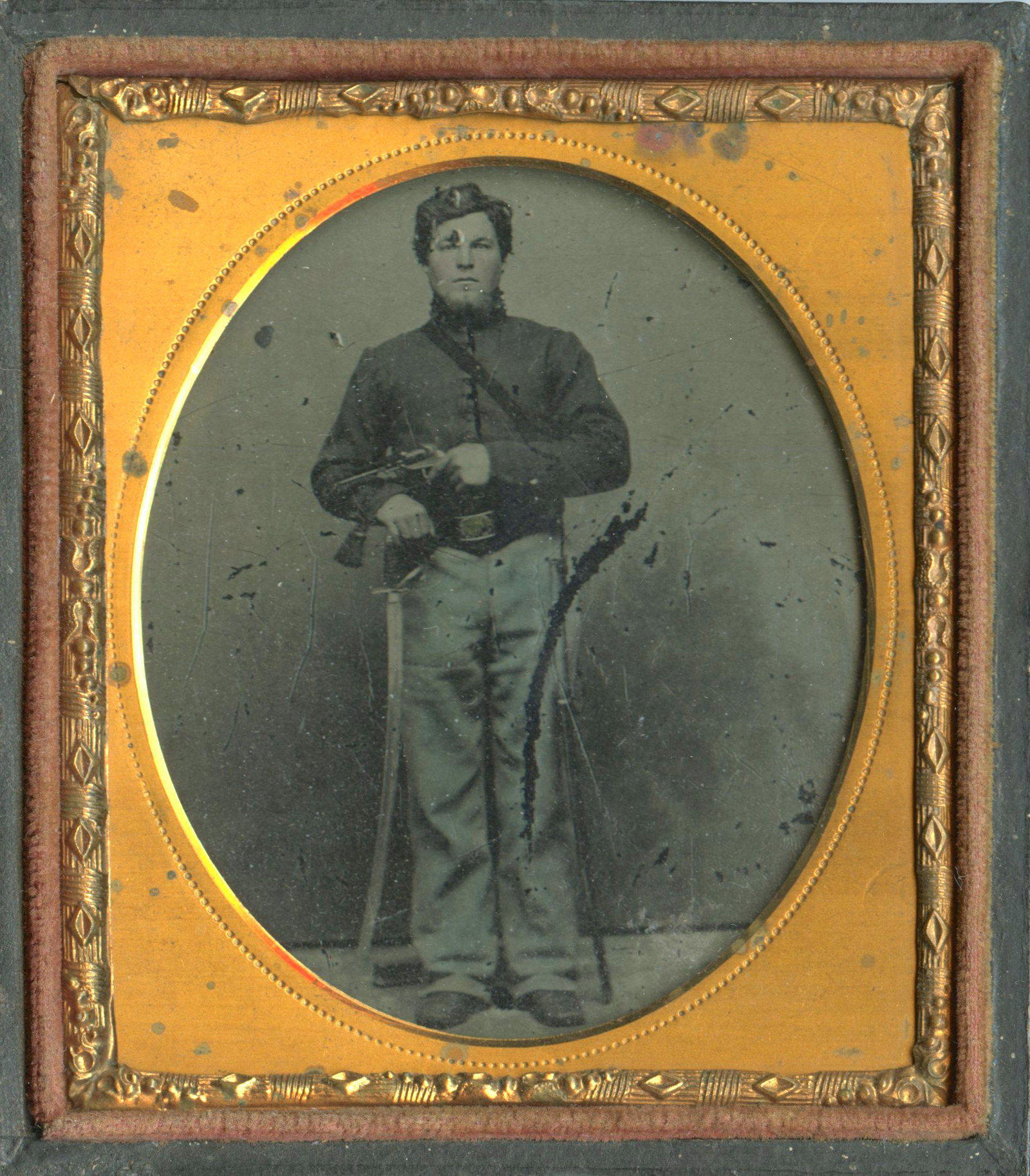 Double-Armed Cavalryman [Tintype]: Sixth plate tintype of a standing Civil War cavalryman who is armed with a saber and pistol. Housed in a full leatherette case. [Civil War, Union, Confederate, Daguerreotype, carte-de-visite, CDV, amb