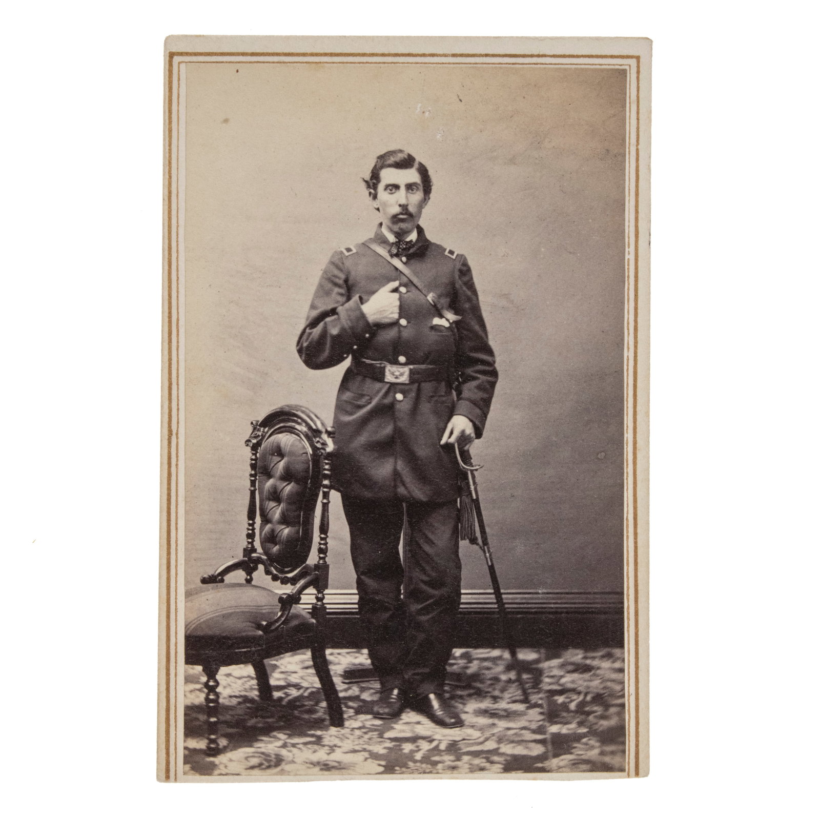 [GETTYSBURG] Gettysburg Casualty Lt. Esbon W. Hindes, Co. F, 1st U.S. Sharp Shooters: An original albumen carte-de-visite full-length studio portrait of an officer standing beside a tufted parlor chair, his left hand resting on the hilt of his foot officer's sword and his right han