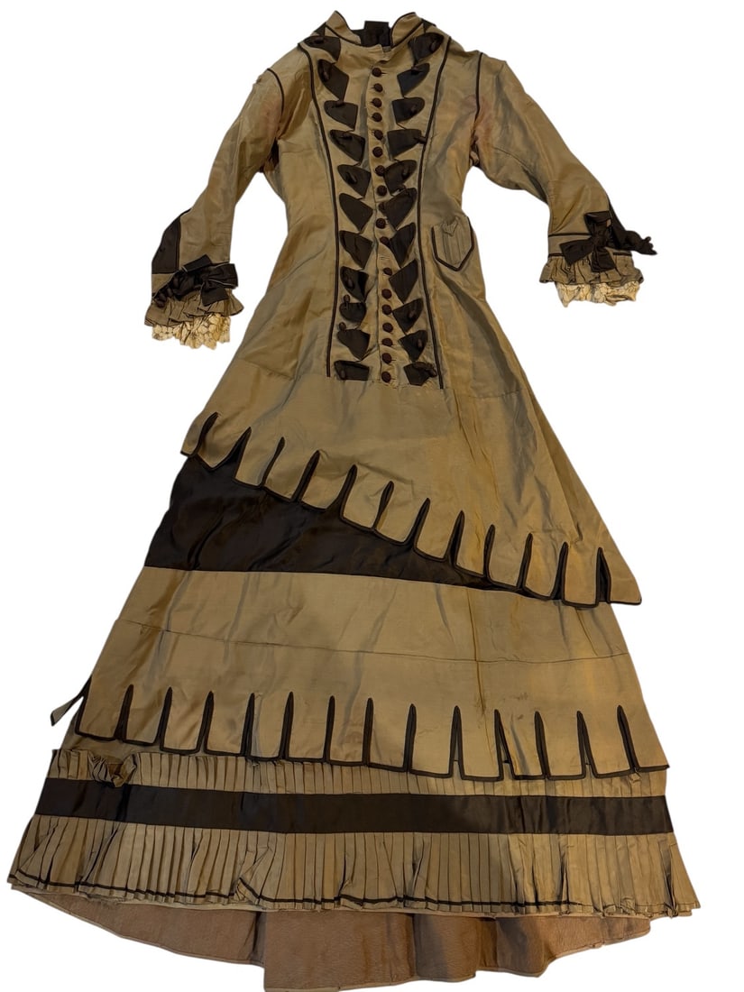 1885 Silk Taffeta Gown: Striking one-piece gown in silk taffeta with contrasting dark brown silk trim and buttons. The fitted collar, hand crocheted buttons, and tassled beads on the front detailing are elegant and unusual. 