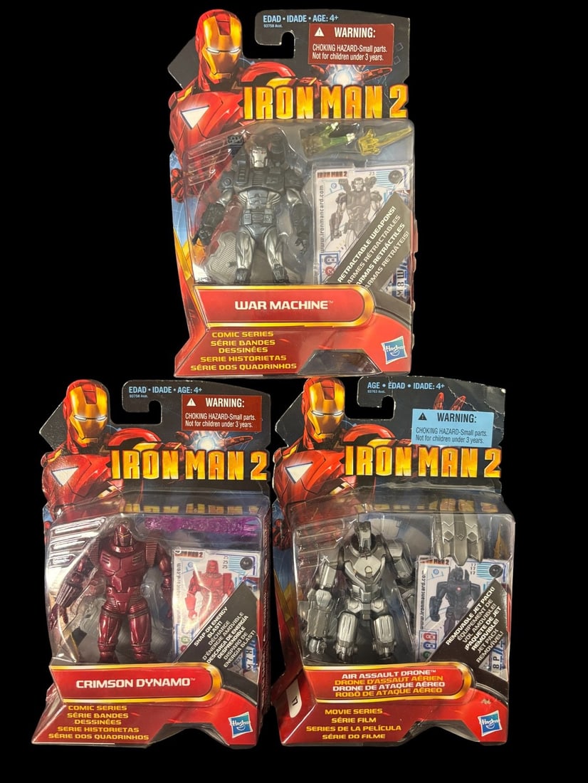 3 Hasbro Iron Man 2 Action Figures: War Machine, Crimson Dynamo, and Air Assault Drone: A group of three Hasbro -Iron Man 2- themed plastic action figures, each sealed in its original, unopened blister packaging with graphic cardboard backing. The lot includes a silver -WAR MACHINE- figu