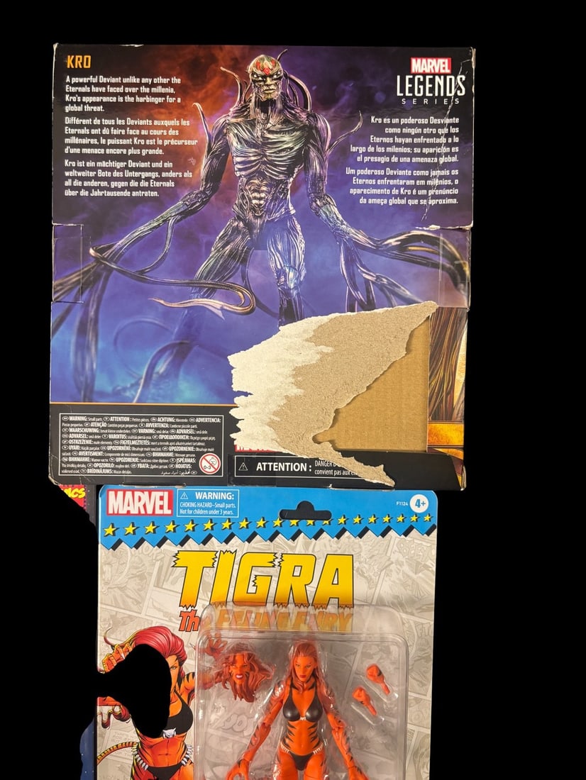A Pair of Hasbro Marvel Legends Action Figures: Kro-eternals Deluxe Series-and Tigra: A pair of Hasbro Marvel Legends action figures. The first figure is Kro, from the Eternals Deluxe Series, depicted as a monstrous, multi-limbed Deviant on its packaging. The box text identifies Kro as