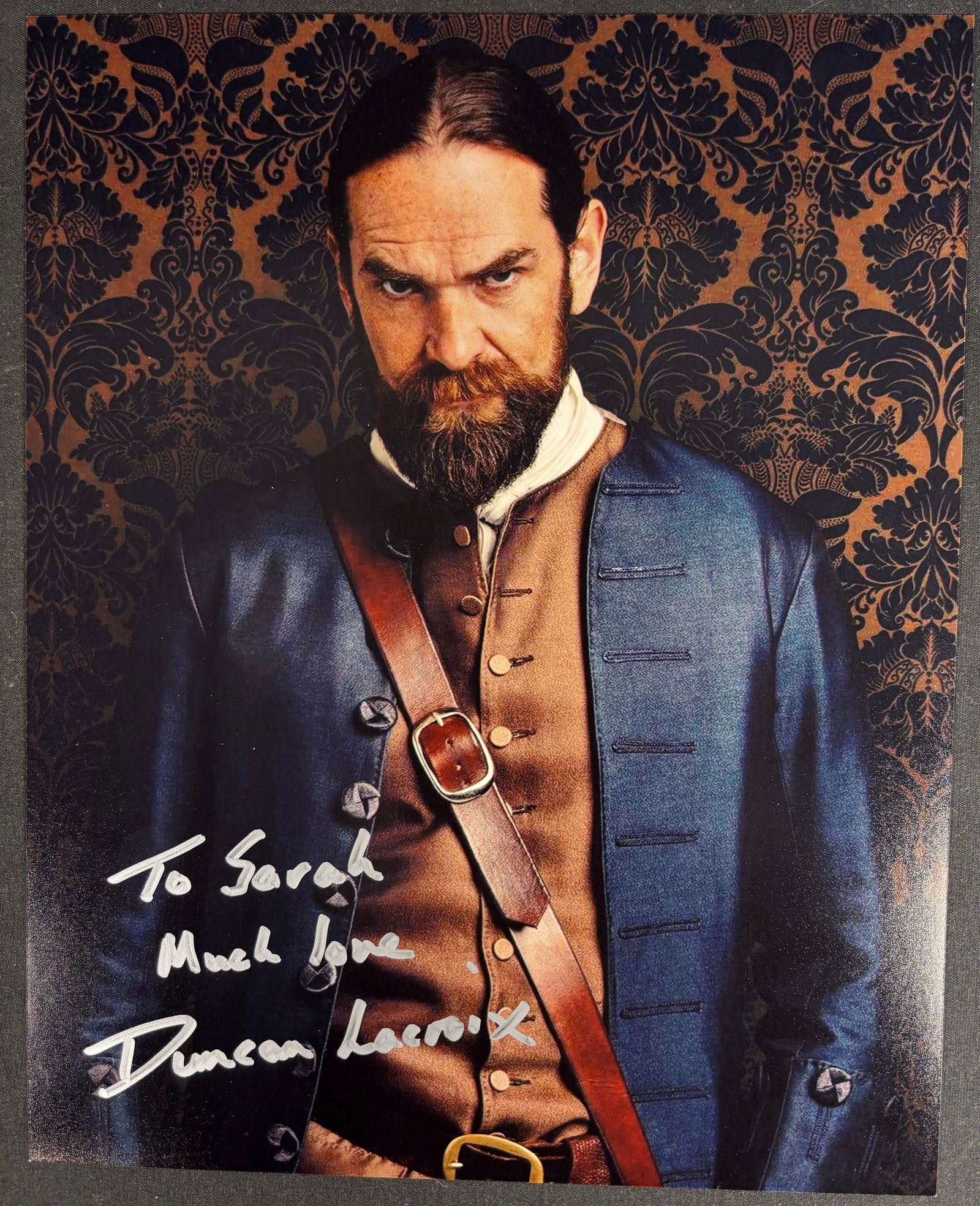 A Signed Color Photograph of Duncan Lacroix as Murtagh Fraser in Outlander: A color photograph on glossy paper depicting actor Duncan Lacroix in character as Murtagh Fitzgibbons Fraser from the television series Outlander. The subject is shown in period costume, including a b