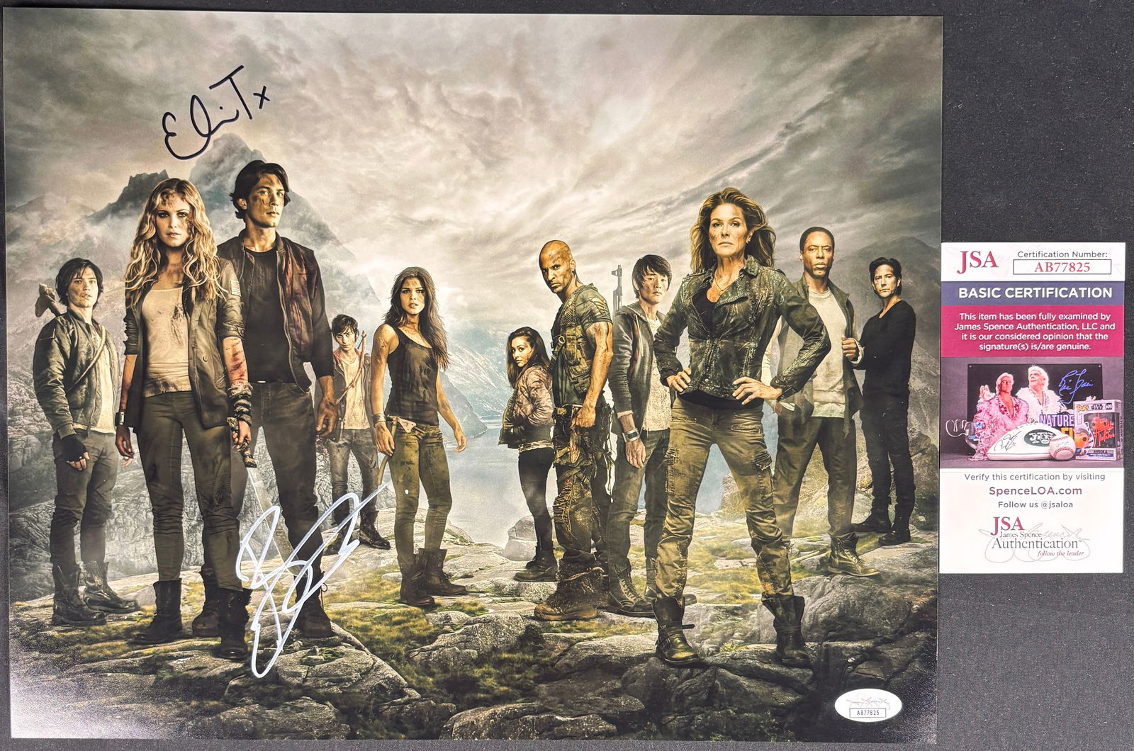 The 100 Cast Signed Promotional Photograph: A color promotional photograph for the television series The 100 depicting the ensemble cast in a rugged landscape. The piece features two signatures, one executed in black marker at the upper left