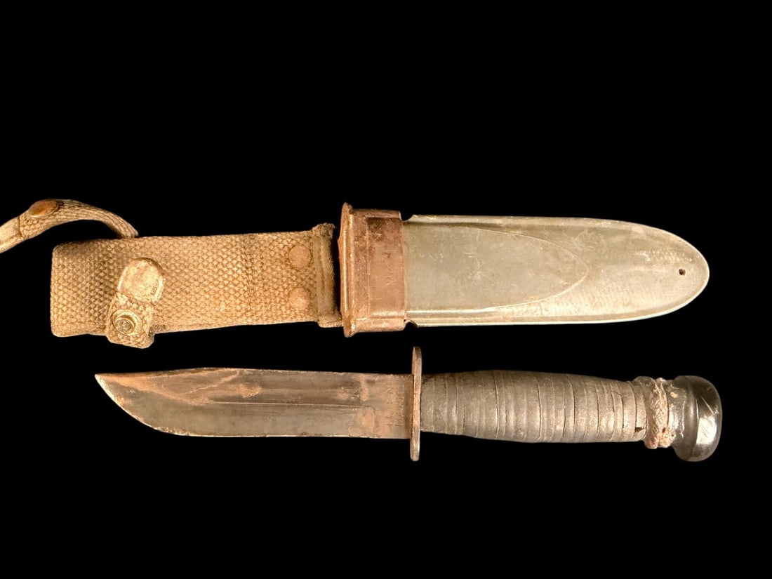 WWII USN MK 1 Fighting Knife: This is a World War II era United States Navy Mark 1 fighting utility knife. The weapon features a steel clip-point blade with a single fuller. The hilt is constructed with a straight steel crossguard