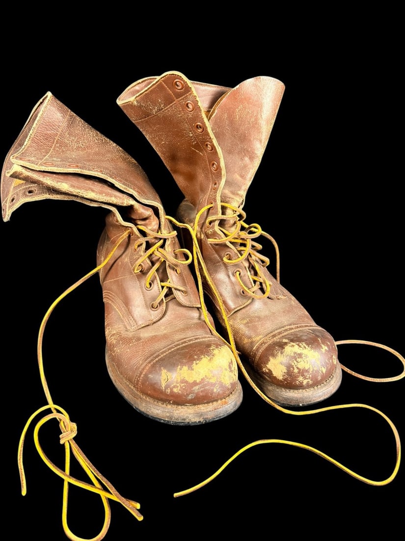 WWII US Army Paratrooper Boots: A pair of original WWII-era US Army paratrooper jump boots manufactured by the International Shoe Co. These boots feature a high-top design in brown leather with a reinforced capped toe and a twelve-e