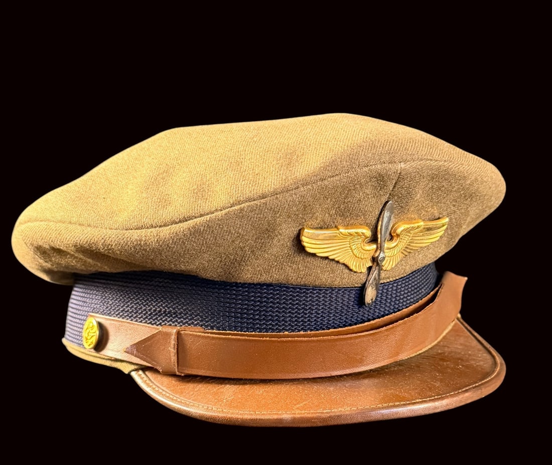 WWII AAF Cadet Cap: This US WWII Army Air Forces Aviation Cadet service cap is constructed with a tan fabric crown and a dark blue textured mohair-style band. The cap features a crusher style softened frame. It is equipp