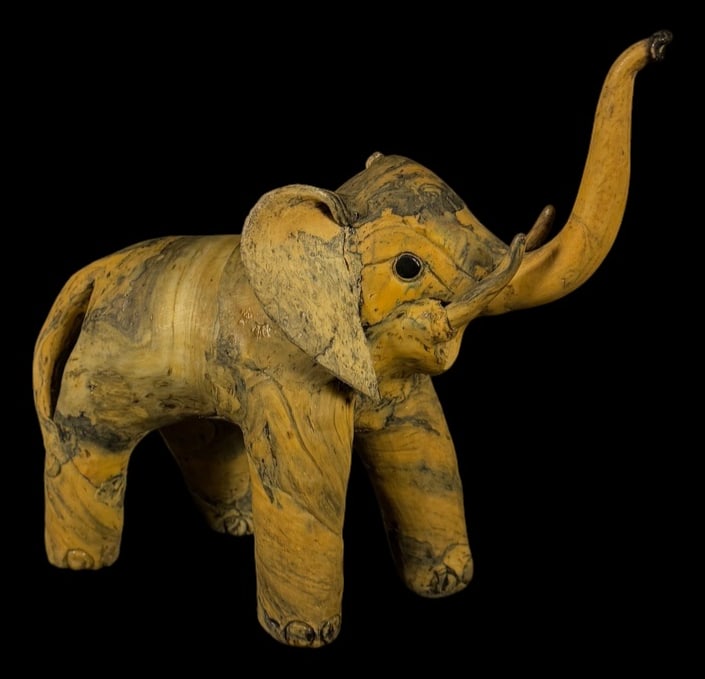 Hand-Carved Elephant Sculpture: Hand-carved elephant sculpture with raised trunk, carved tusks, and natural marbled wood-grain appearance.
