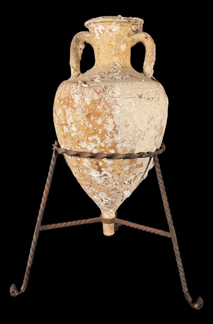 Barnacle-Encrusted Amphora Display: Decorative amphora-style pottery vessel with marine encrustation displayed on a iron stand. Coastal or Mediterranean-inspired décor piece. 32" x 22"