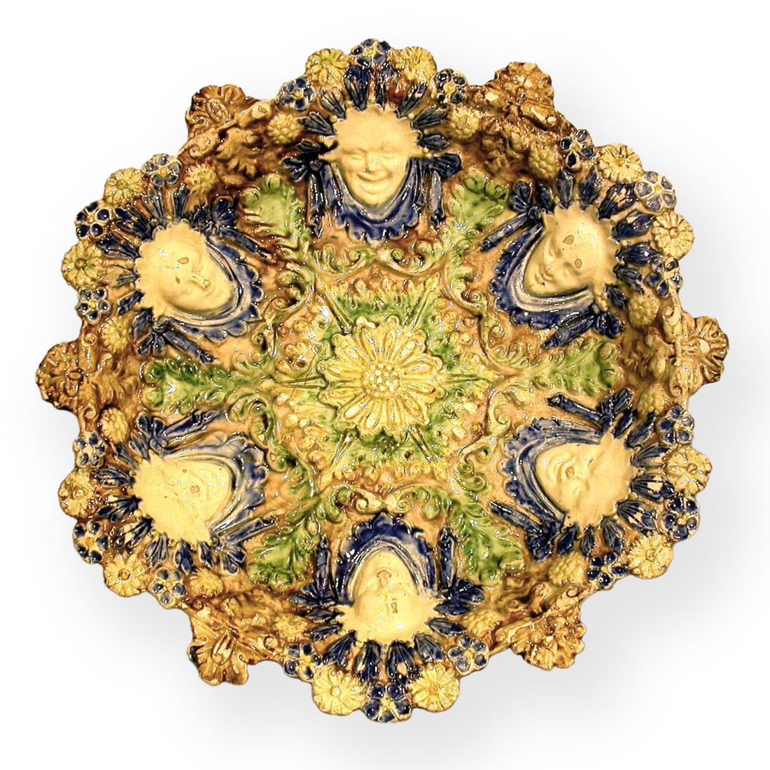 COUPE, XIXe SIÈCLE: COUPE, XIXe SIÈCLE circulaire à bord dentelé en terre vernissée dans le style post-Palissy ornée en relief, en alternance, de masques grimaçants et souriants, fleurettes,