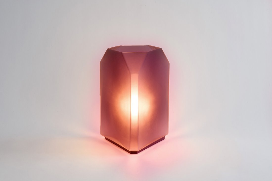 Tyler Table Lamp in Burgundy Glass by Egg Collective: A one-off color-way of Egg Collective's faceted glass Tyler Table Lamp. Perched upon a base of blackened white oak, the deep rose colored glass surround casts a moody yet tranquil glow. Hand-blown gla