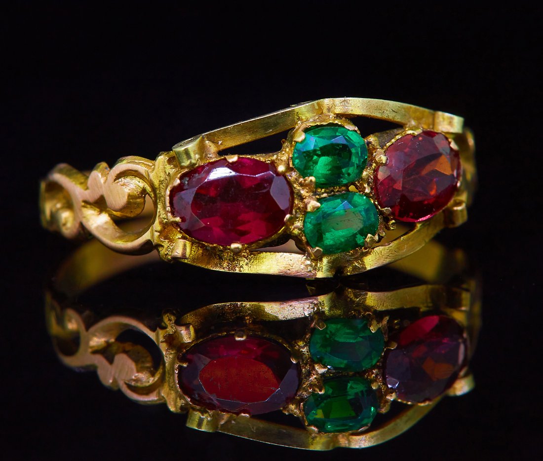 ANTIQUE EMERALD AND GARNET RING: ANTIQUE EMERALD AND GARNET RING, set with 2 emeralds, flanked with a garnet on the sides. With openwork scrolling shoulders. The band with scrolling engraving. Size Q. 1.5 grams.
